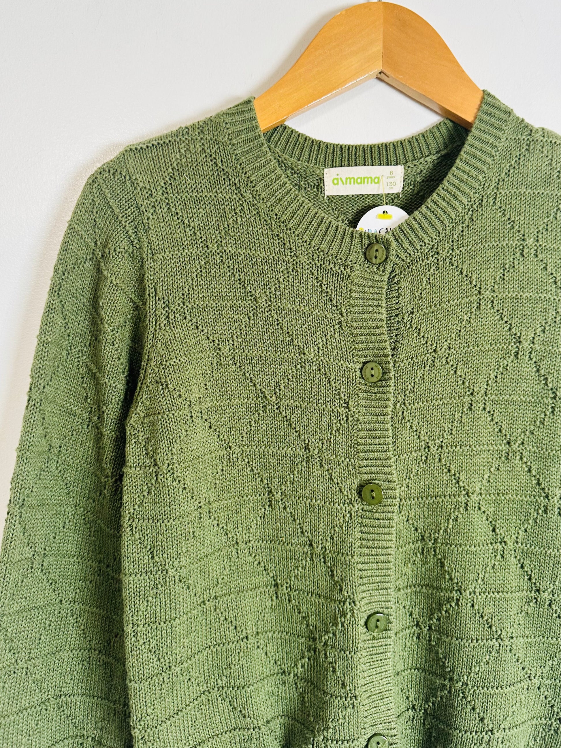 Green knitted cardigan with button details on a wooden hanger against a white background