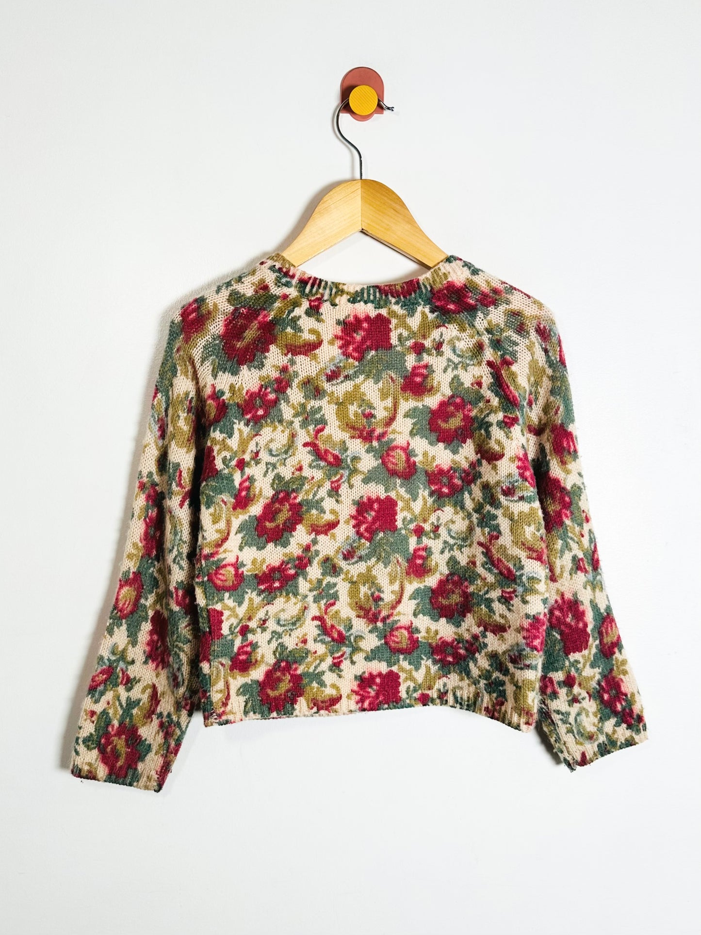 Floral-patterned sweater on a hanger against a white background