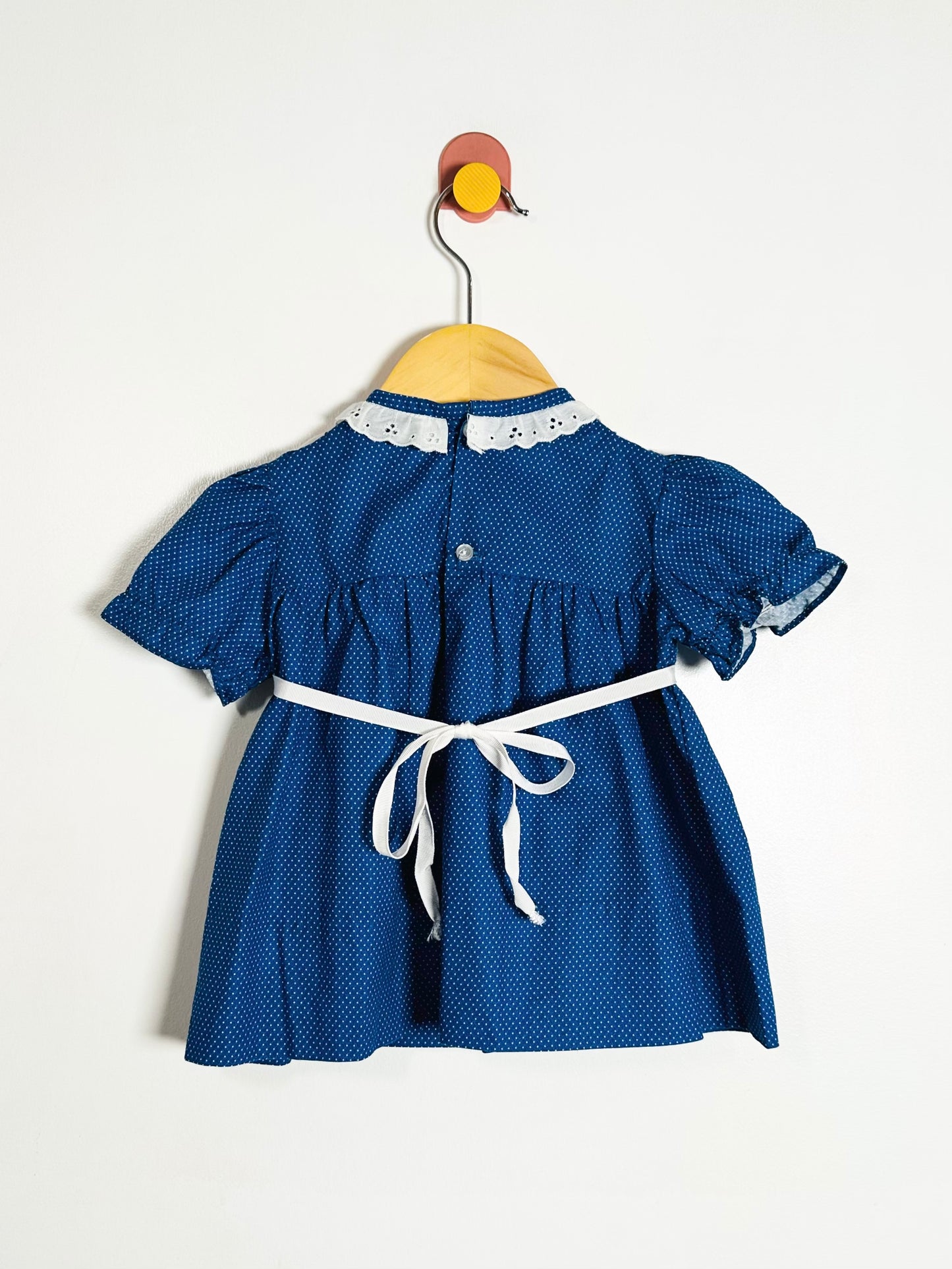 Blue dress with white lace collar and belt on a hanger against a white background