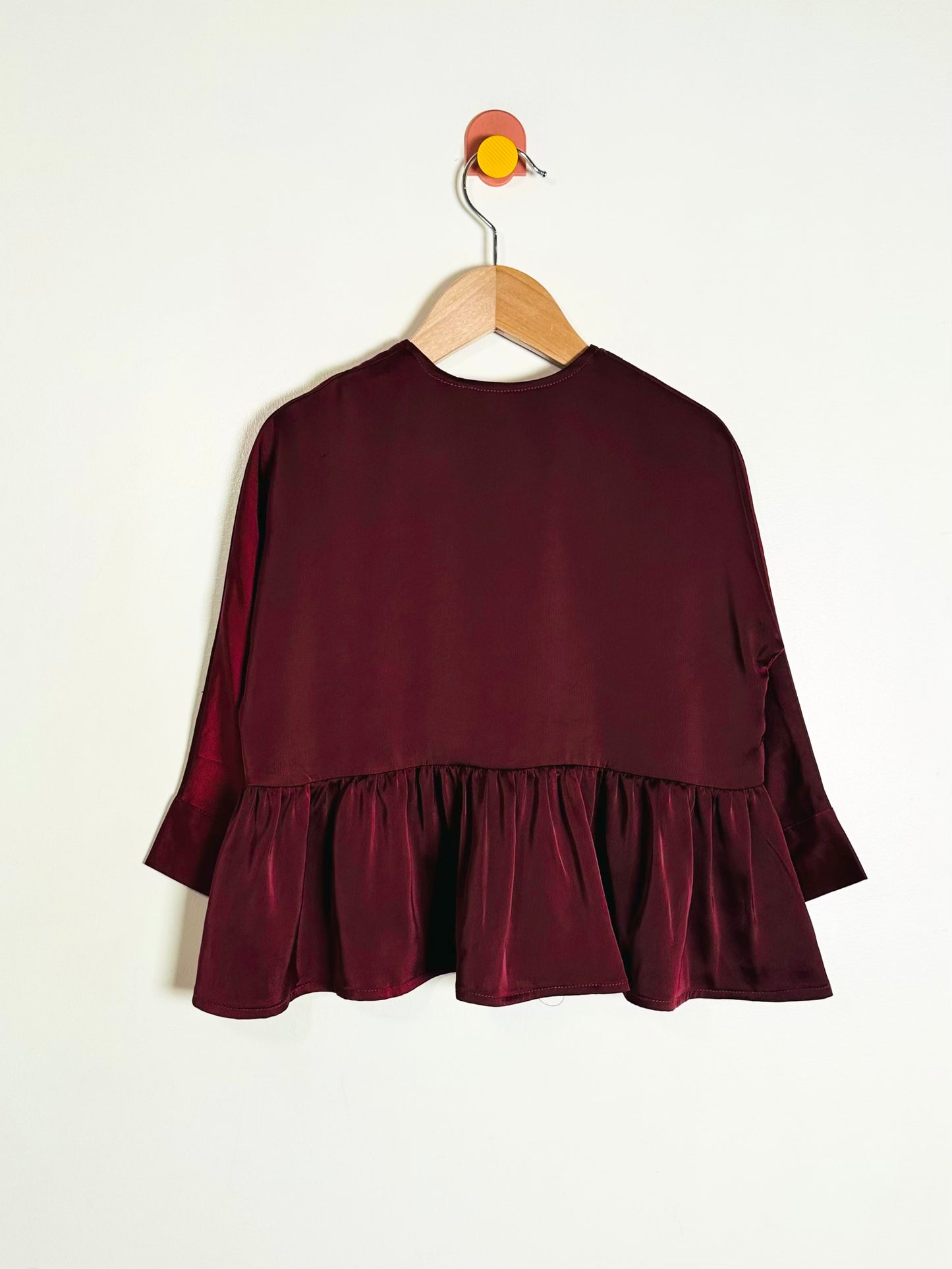 Maroon blouse with ruffled bottom hanging on a wooden hanger against a white background