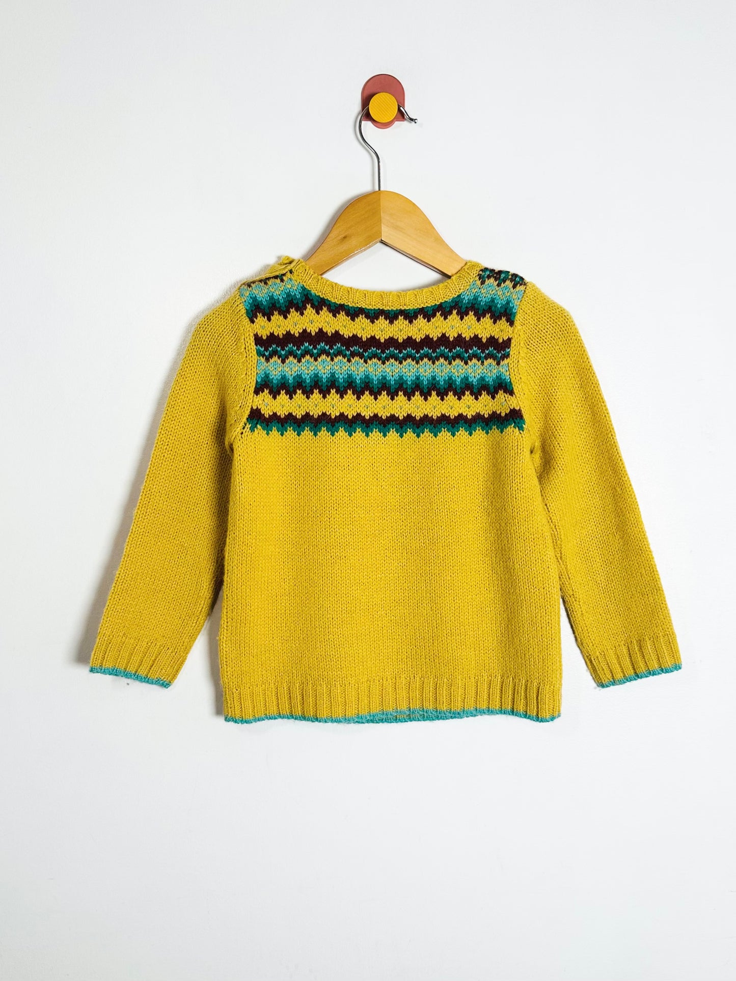 Yellow sweater with a patterned neckline on a hanger against a white background