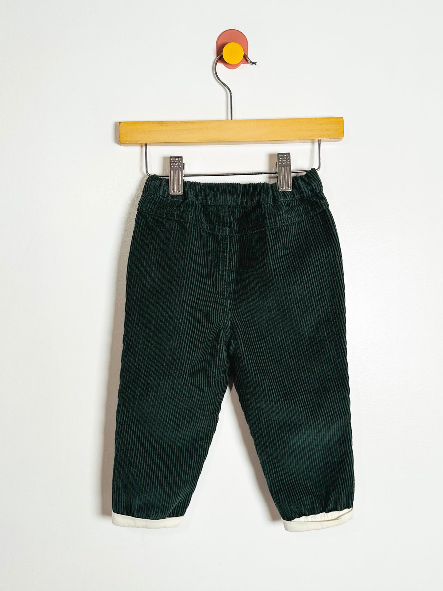 Green corduroy pants on a wooden hanger against a white background