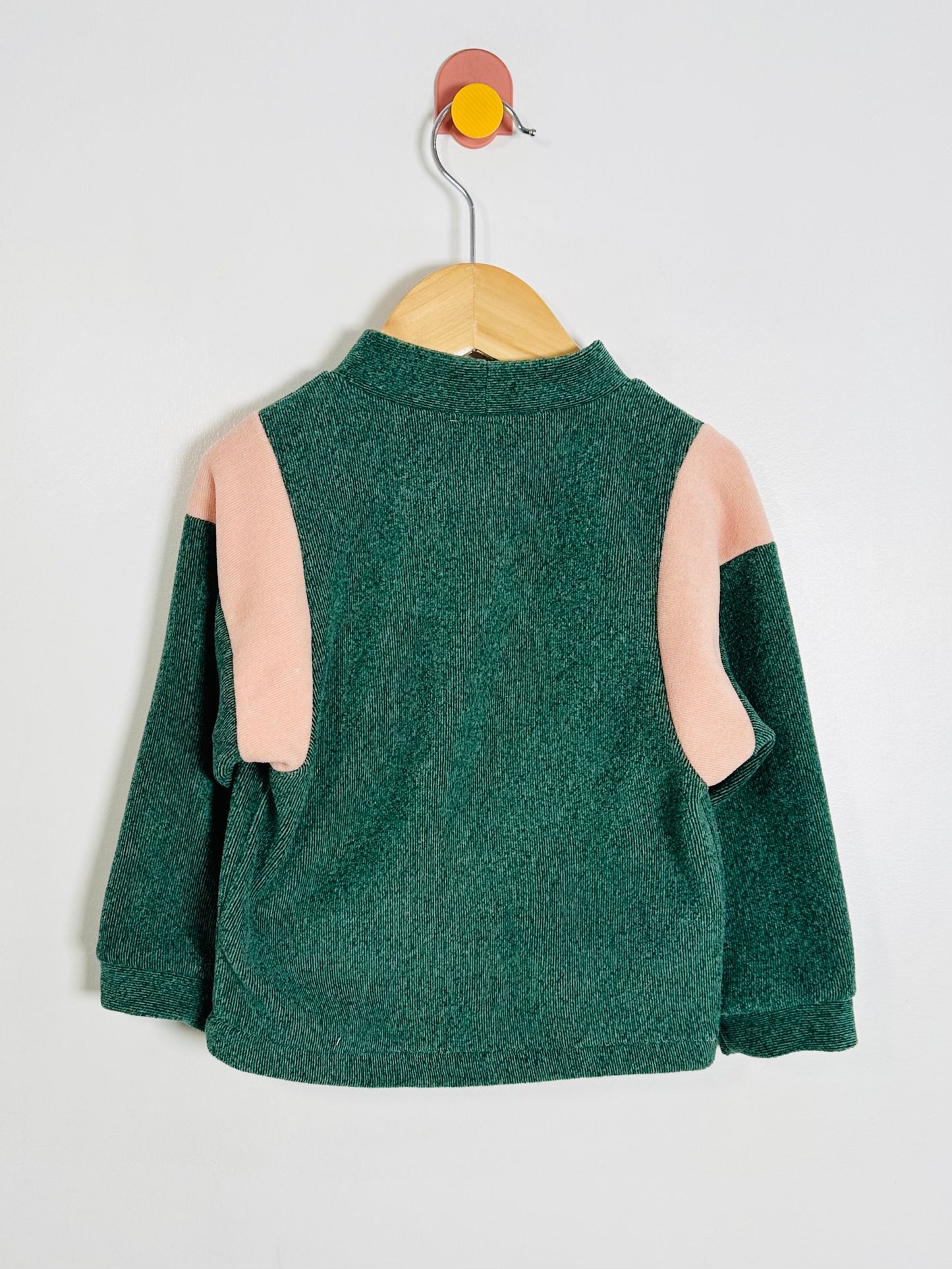 Green fleece sweater with pink sleeves on a hanger against a white background