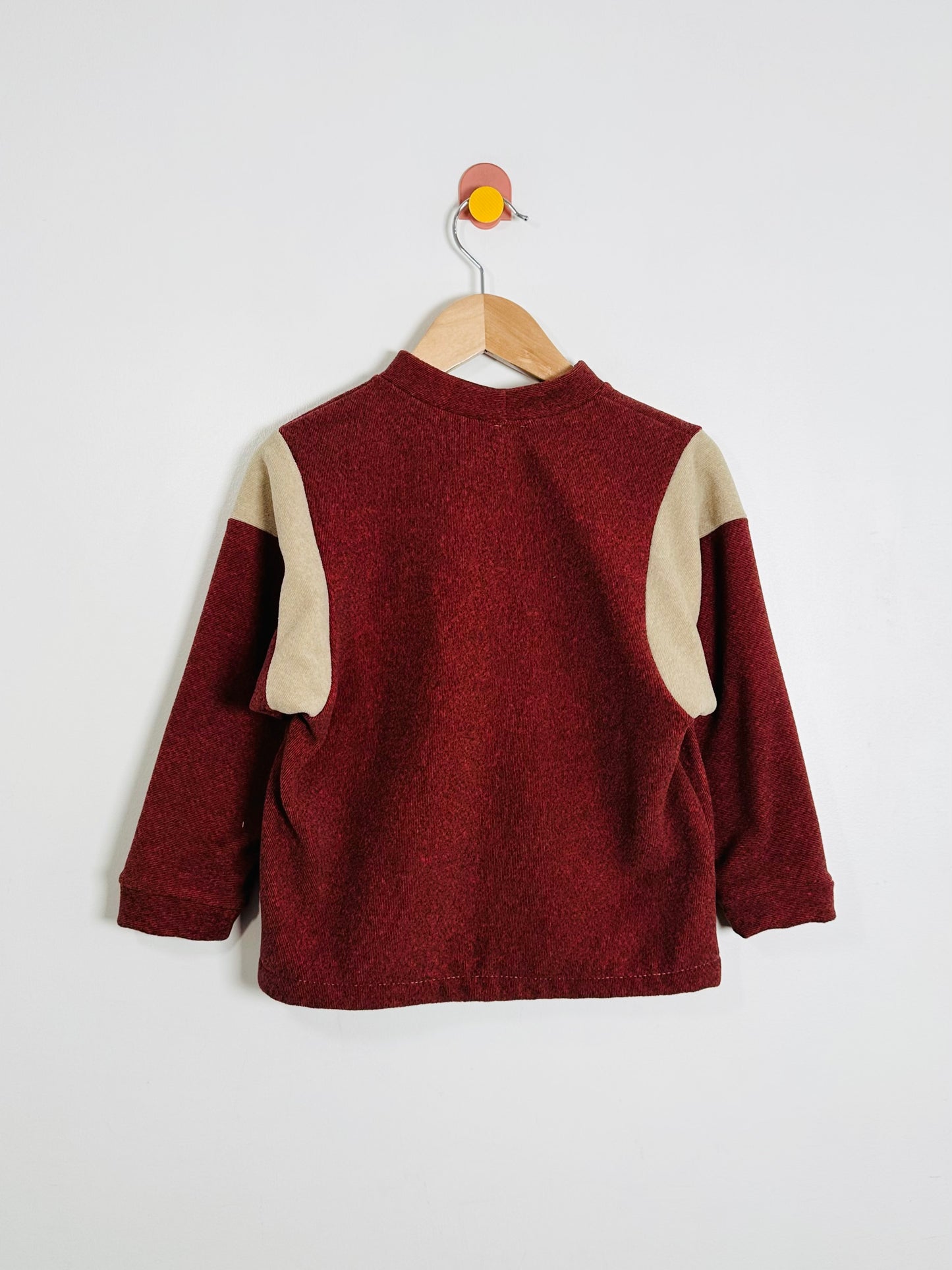 Maroon sweater with beige sleeves on a hanger against a white background