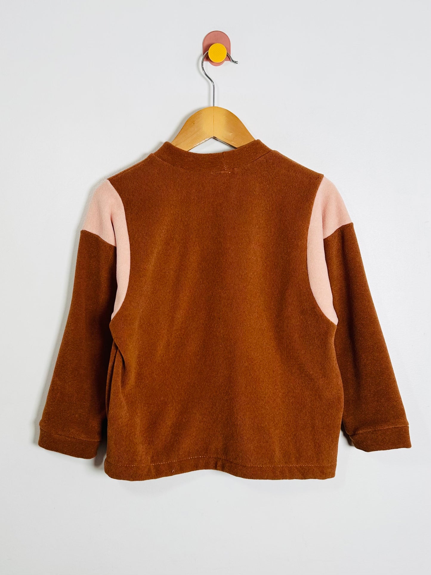 Brown children's jacket with pink accents on a hanger against a white background
