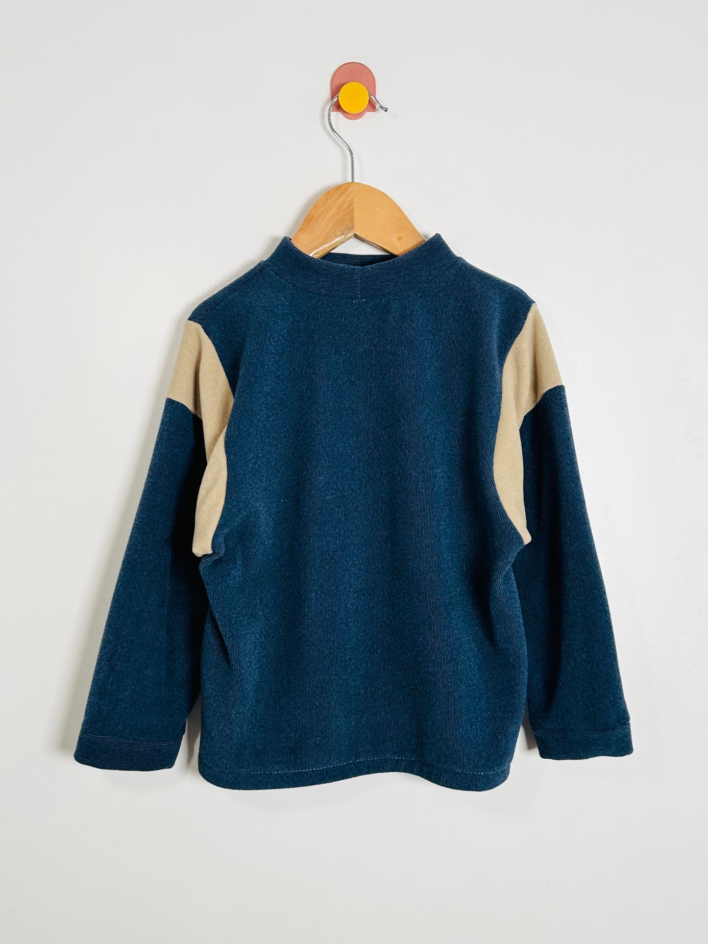 Blue and beige fleece pullover on a wooden hanger against a white background