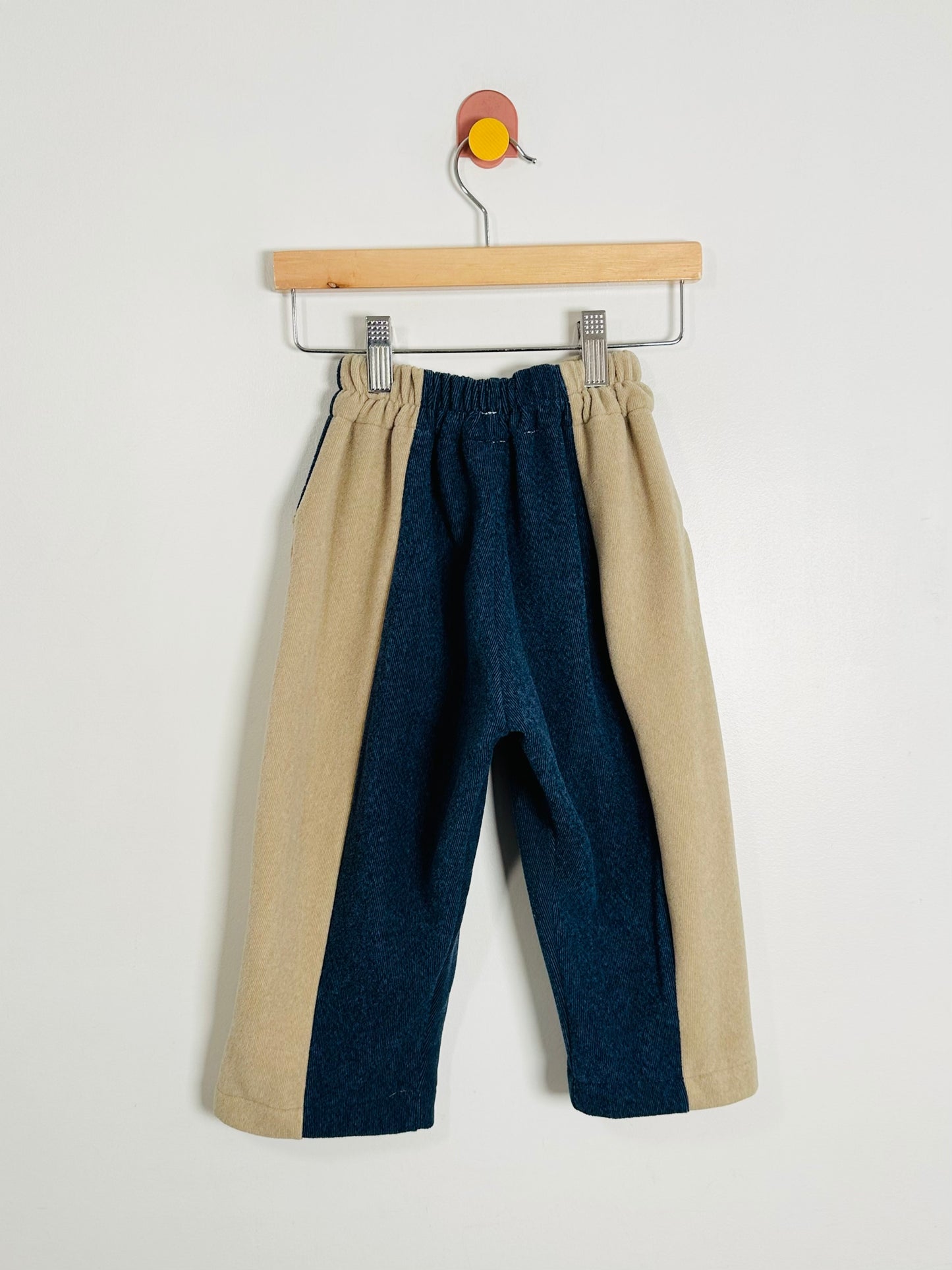 Two-tone pants with beige and blue colors on a hanger against a white background