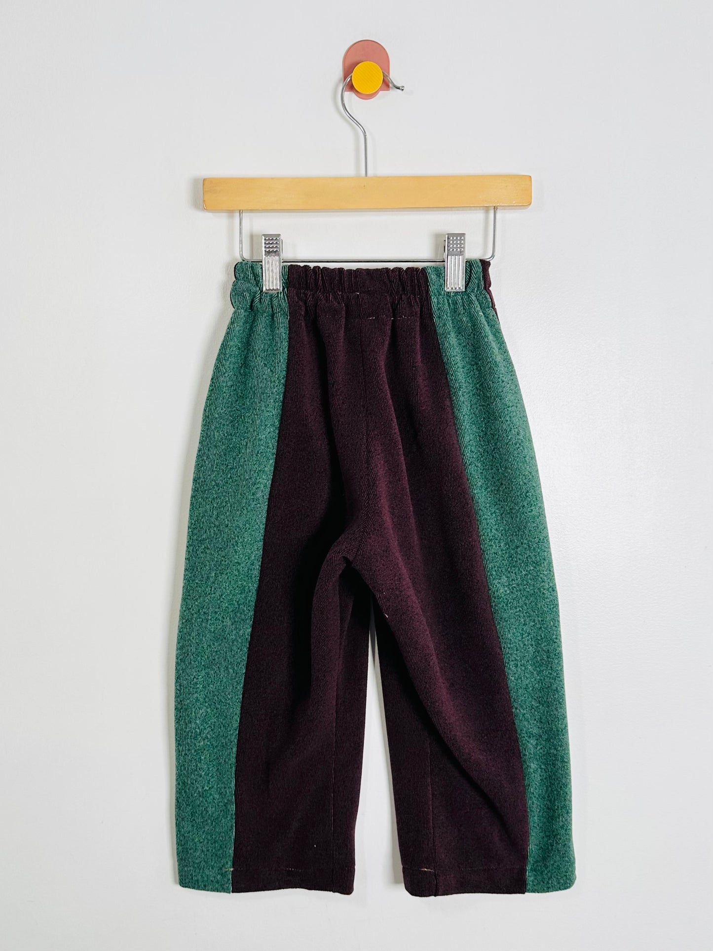Two-tone pants with green and purple on a hanger against a white background