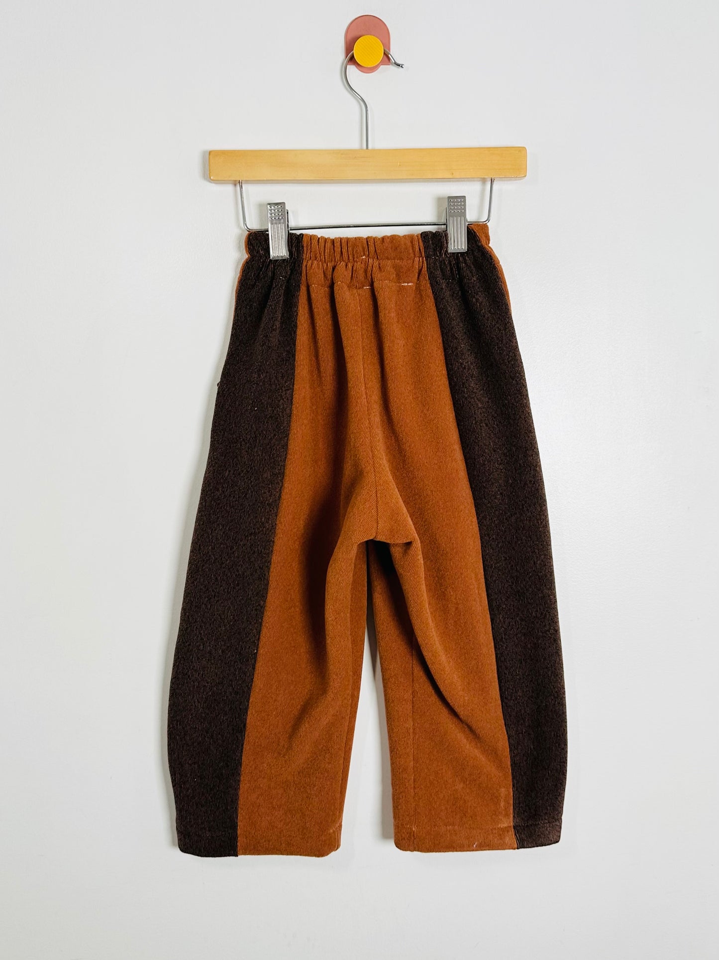 Brown and orange pants on a hanger against a white background