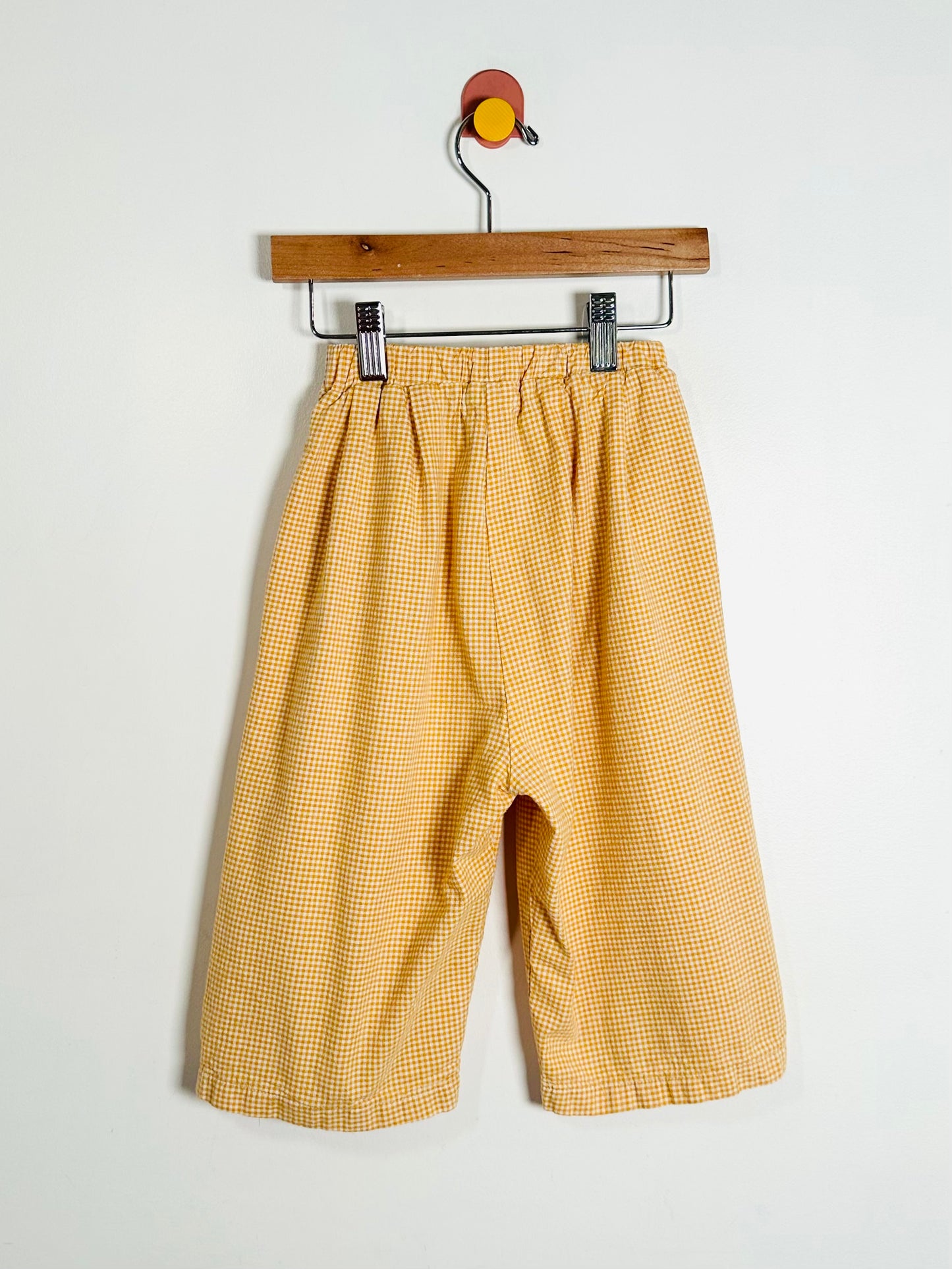 Yellow checkered pants on a hanger against a white background