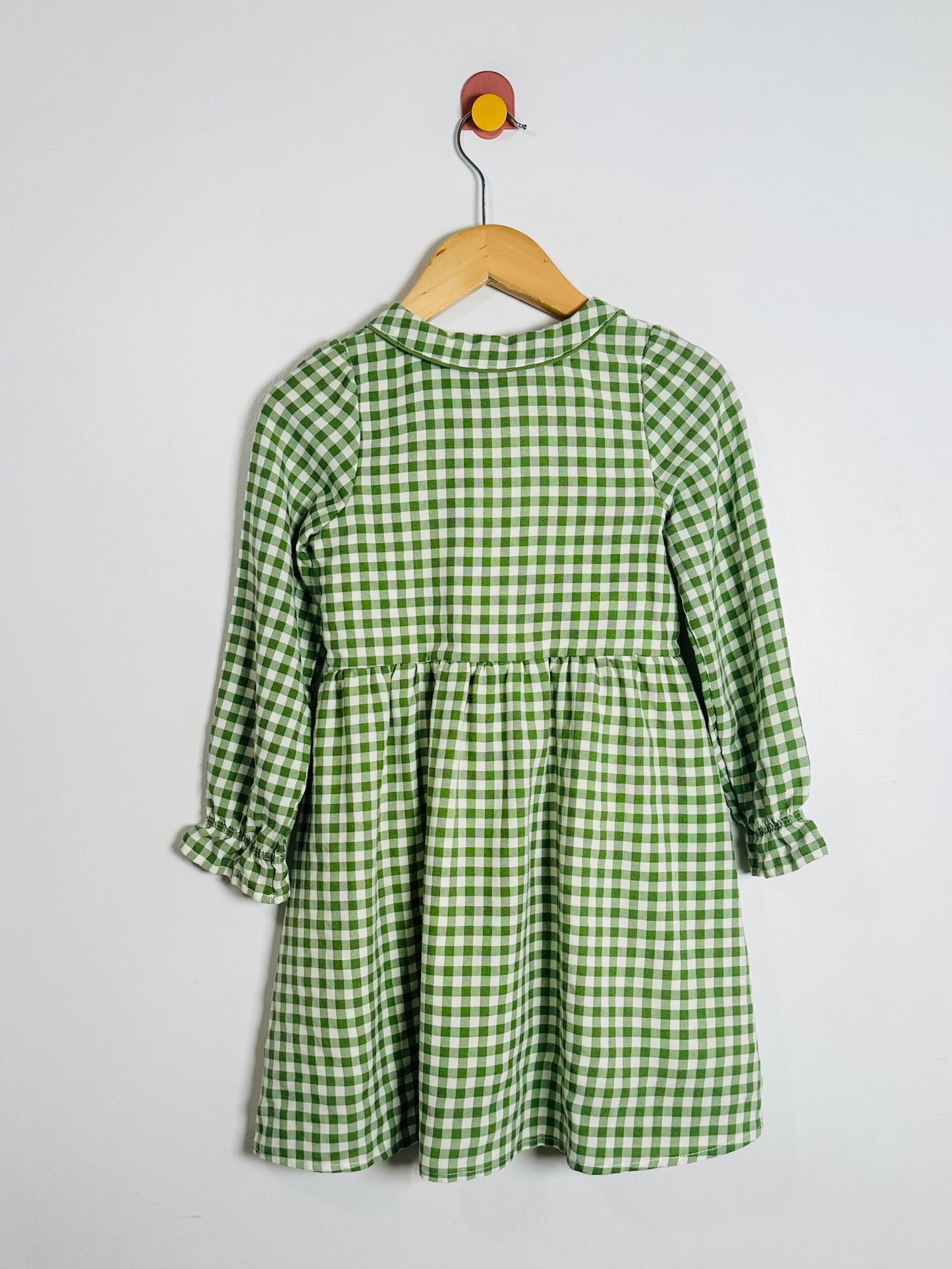 Green checkered dress on a hanger against a white background