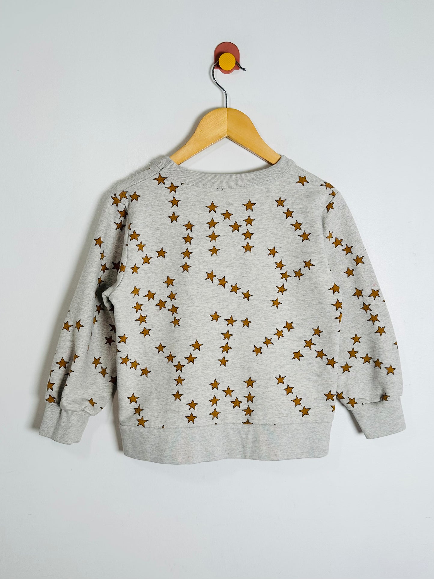 Gray sweatshirt with star pattern on a wooden hanger against a white background