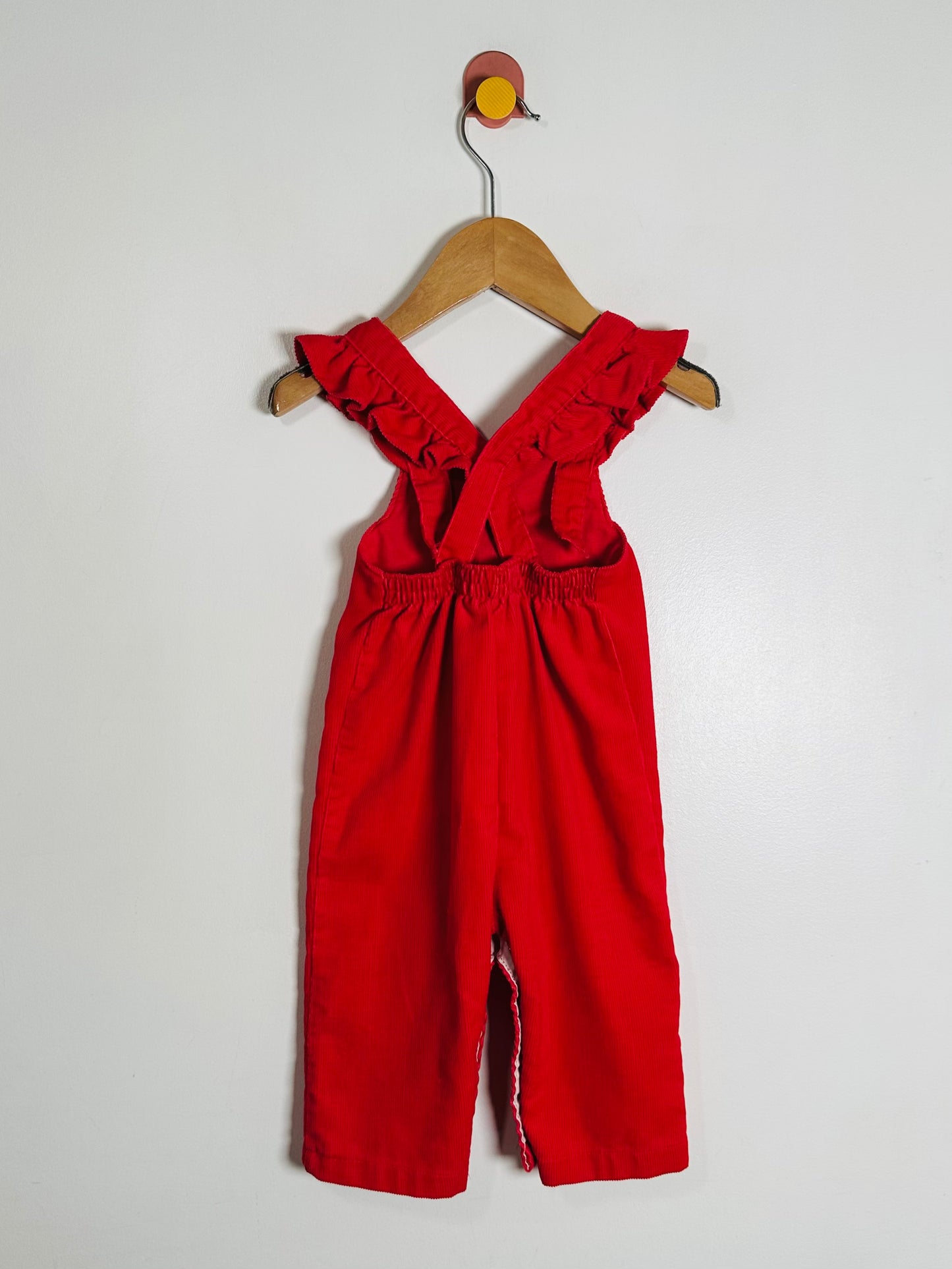 Red jumpsuit with ruffled straps on a wooden hanger against a white background