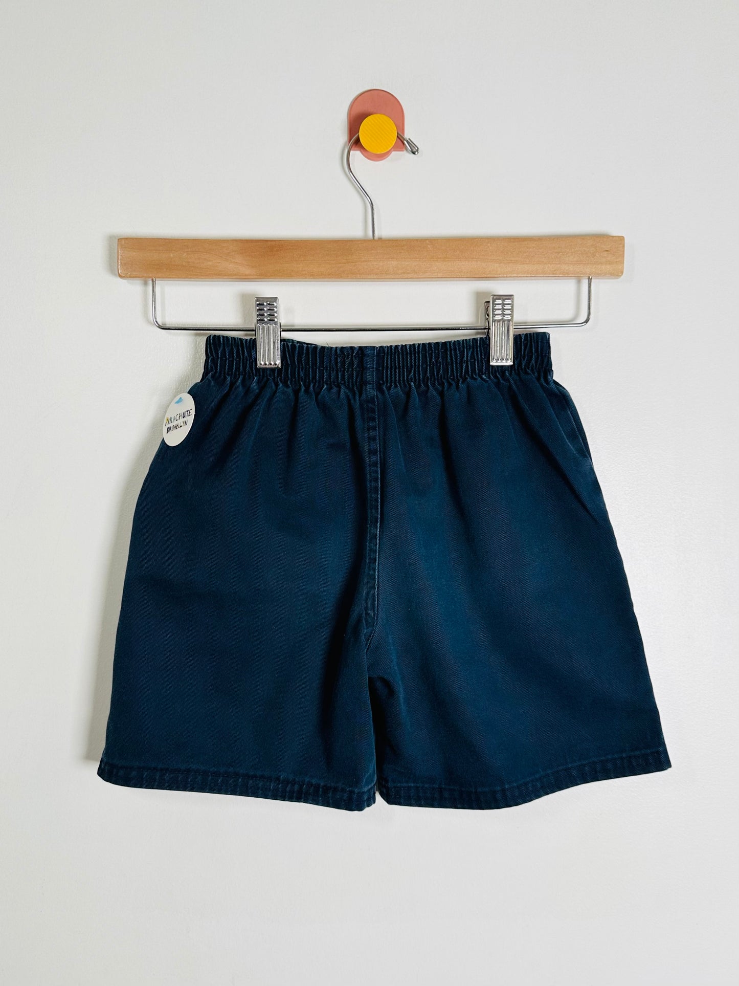 Navy blue shorts on a wooden hanger against a white background