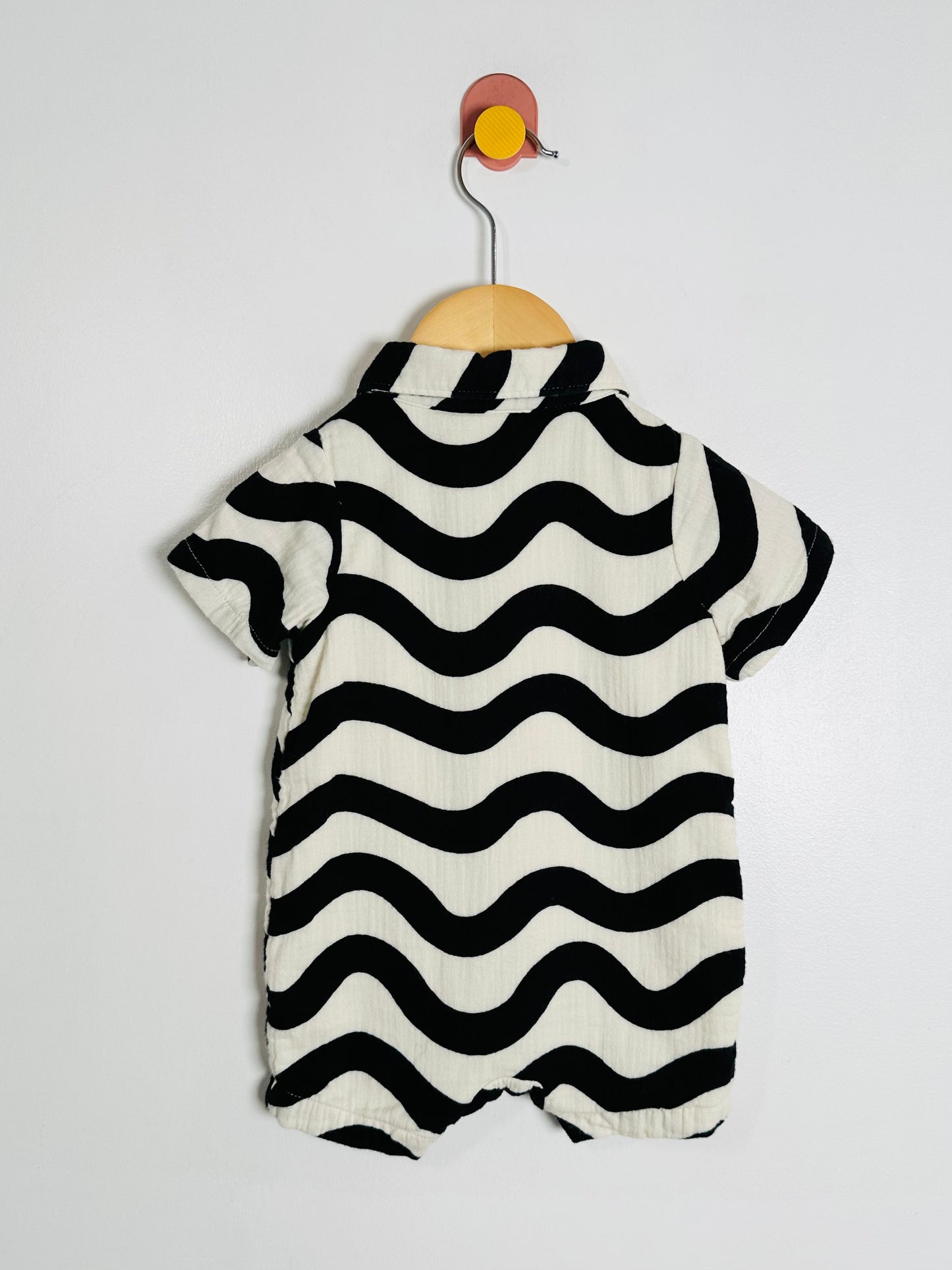 Black and white striped baby romper on a hanger against a light gray background