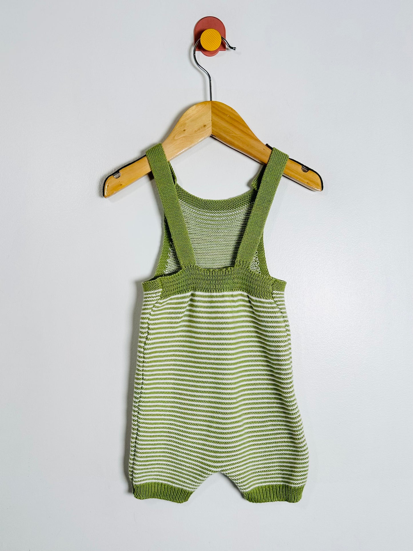 Green striped baby romper with suspenders on a wooden hanger against a white background