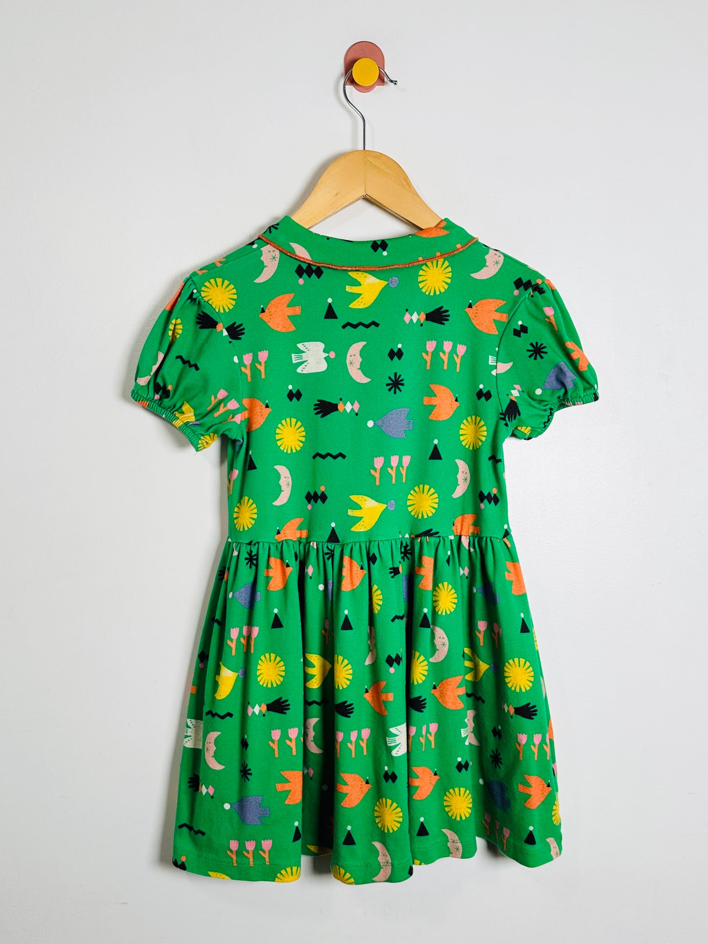 Green dress with colorful patterns on a hanger against a white background