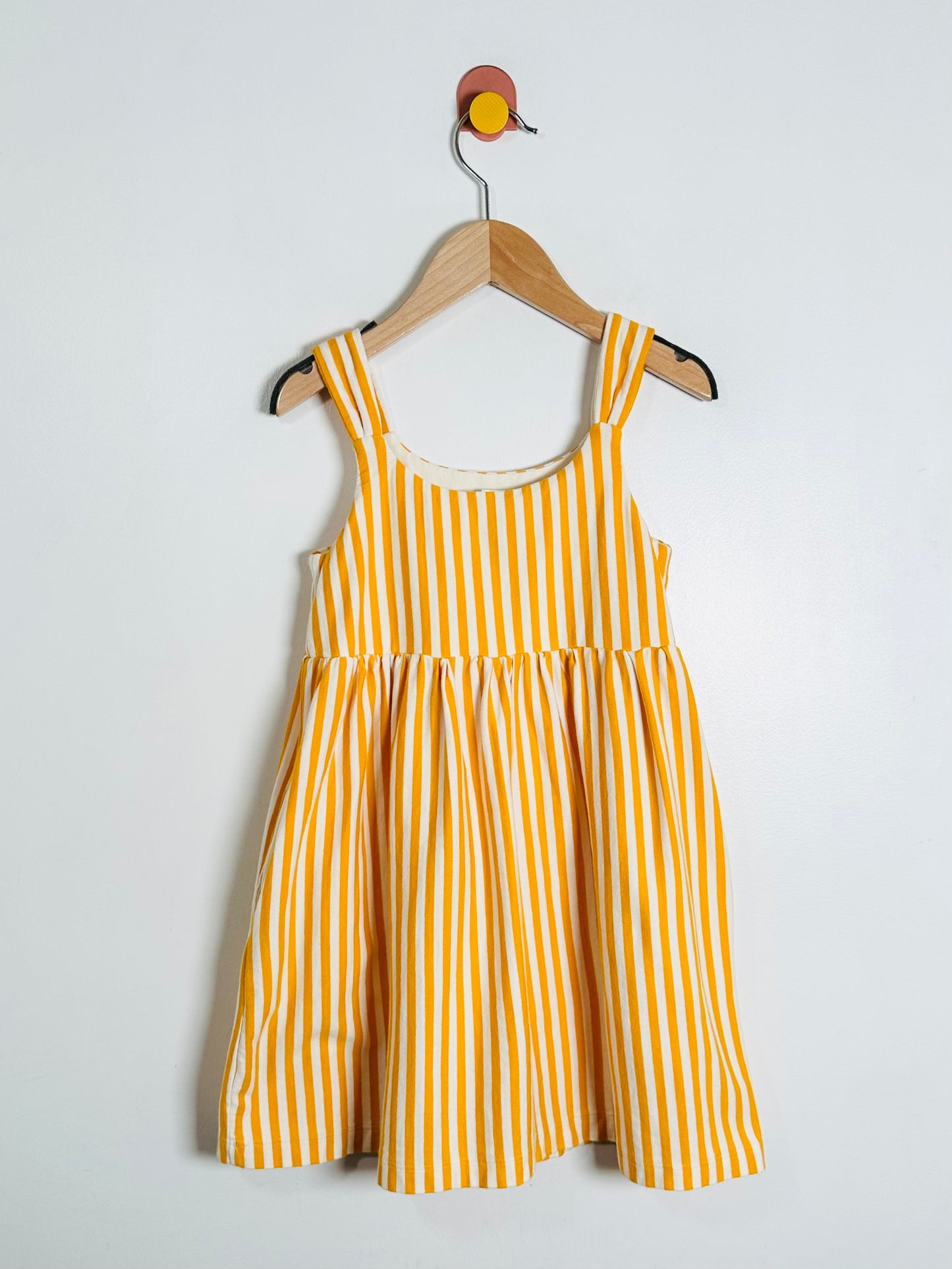 Yellow and white striped dress on a hanger against a light gray background
