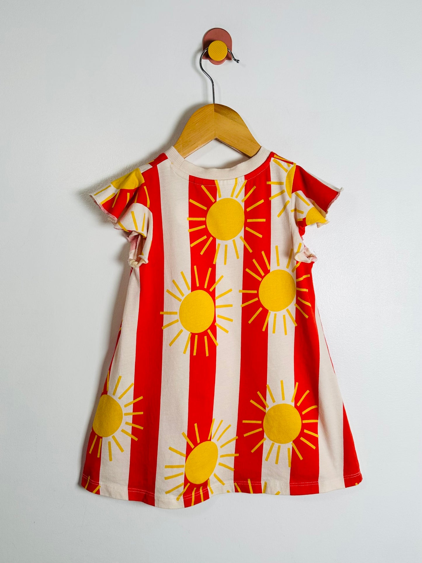 Children's dress with sun pattern on a hanger against a white background