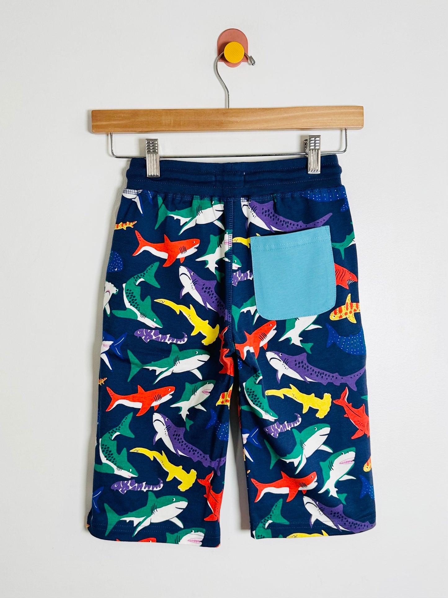 Children's shorts with shark pattern on a hanger against a white background