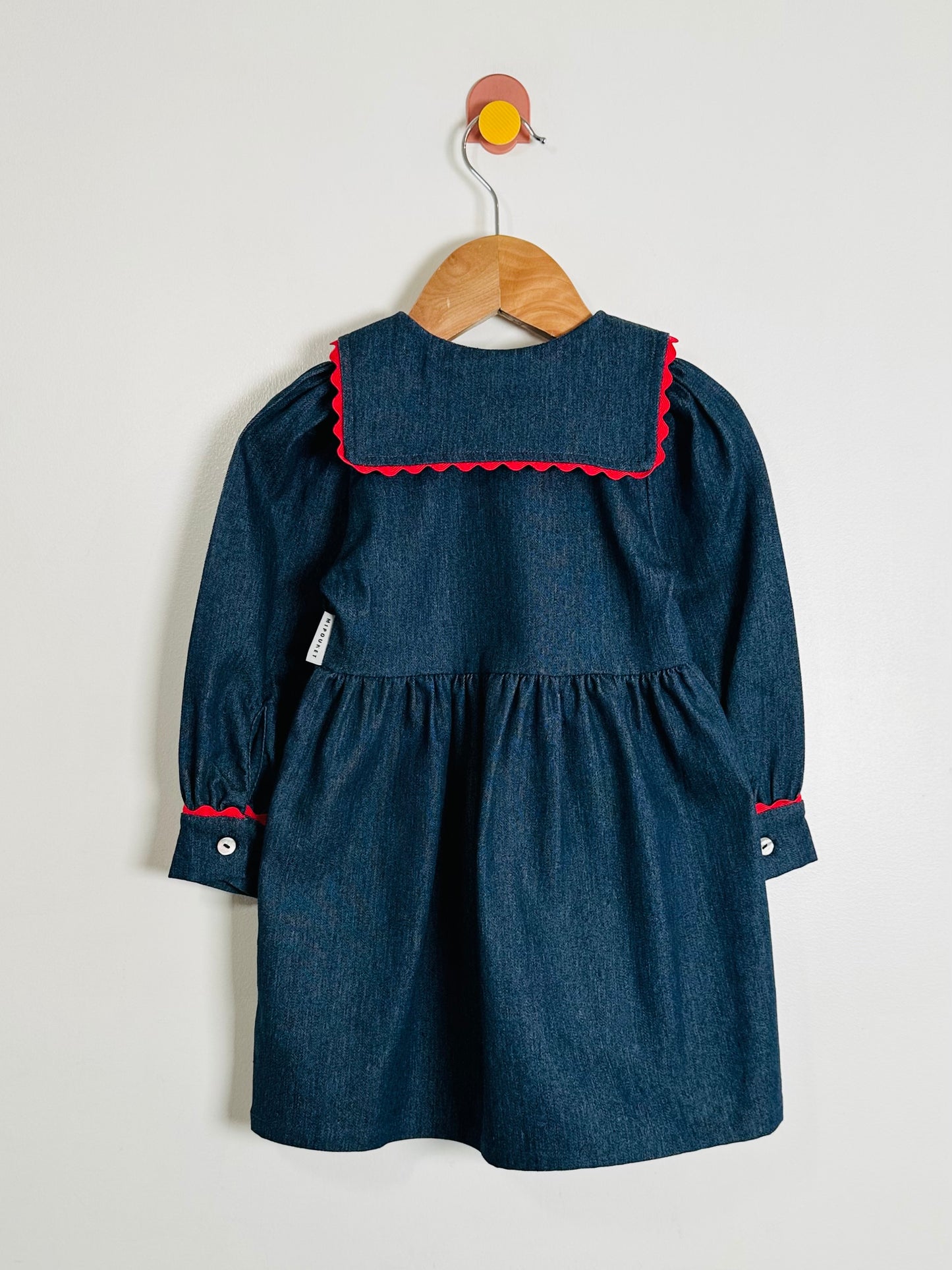 Blue dress with red trim on a wooden hanger against a white background