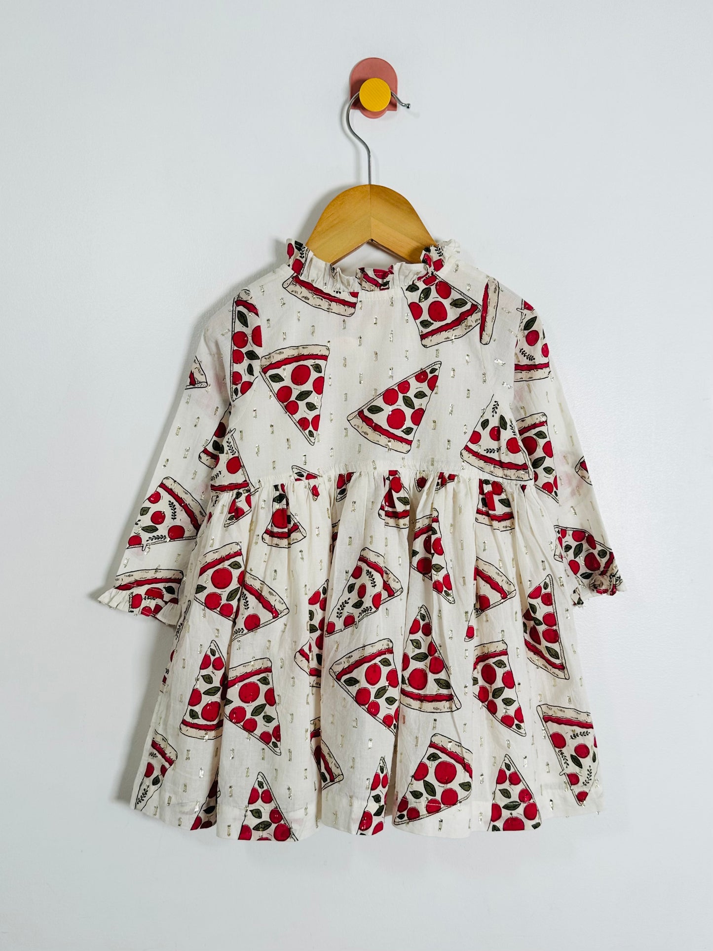Children's dress with pizza print on a hanger against a white background
