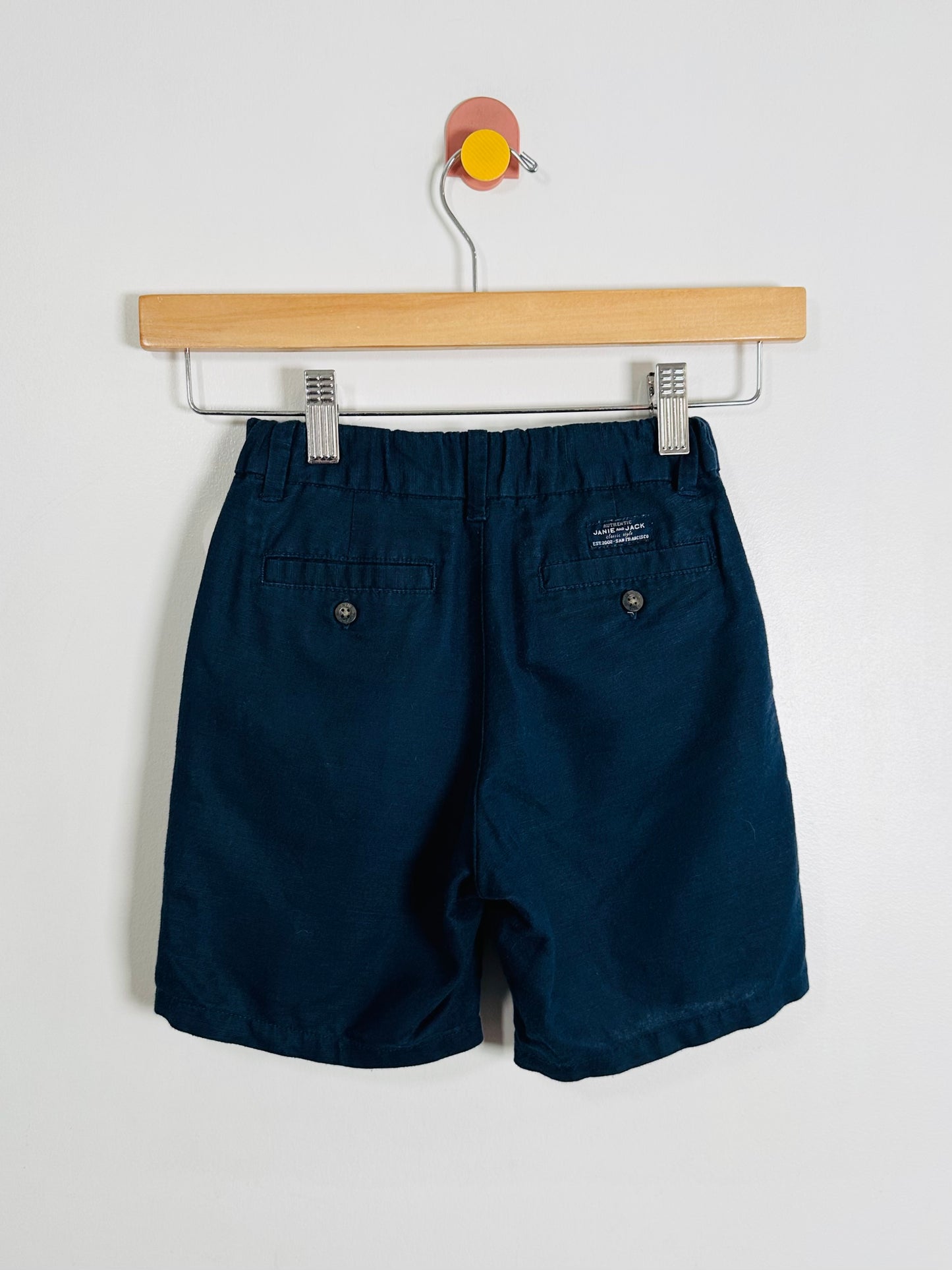 Navy blue shorts hanging on a wooden hanger against a white background