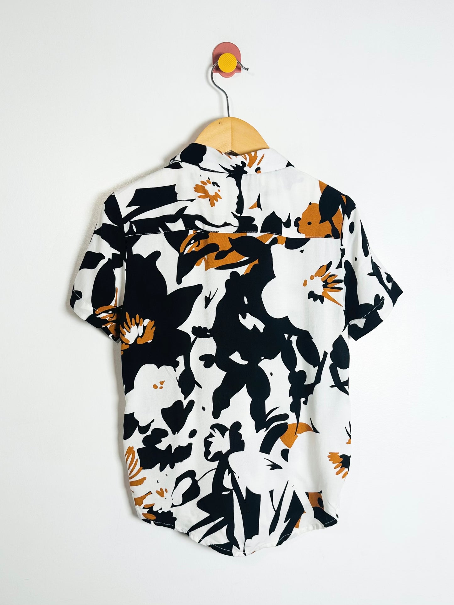 Short-sleeve shirt with black and white abstract pattern on a hanger against a white background