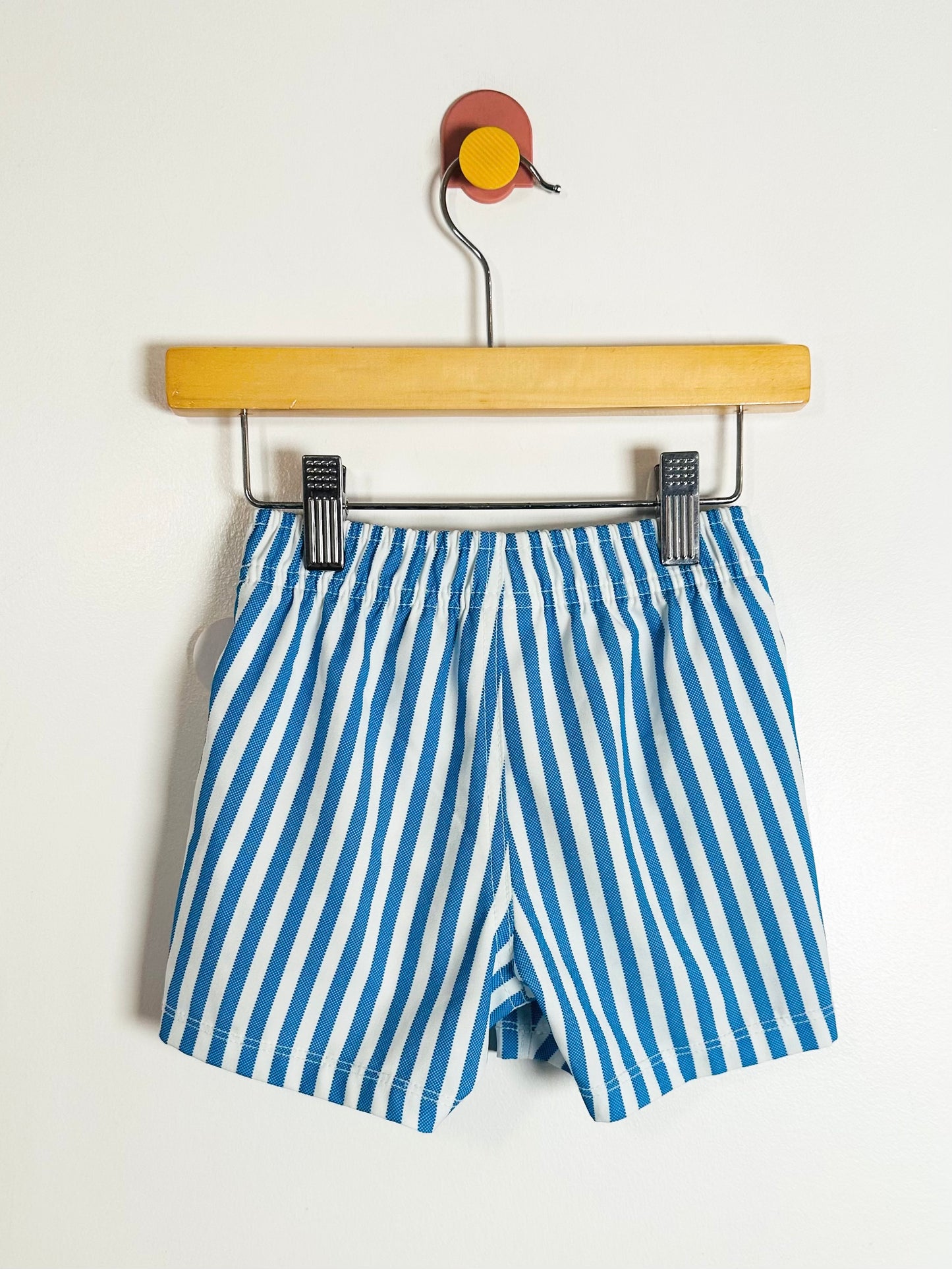 Blue and white striped shorts on a wooden hanger against a white background