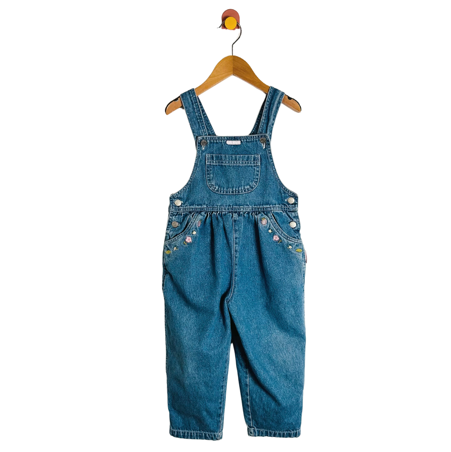 Blue denim overalls on a wooden hanger against a white background