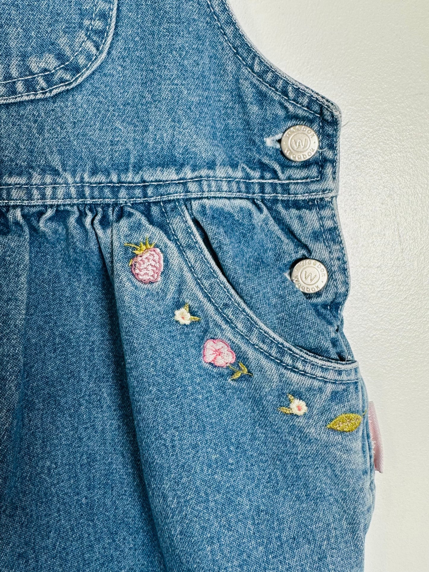 Blue denim overalls with floral patches on a light gray background