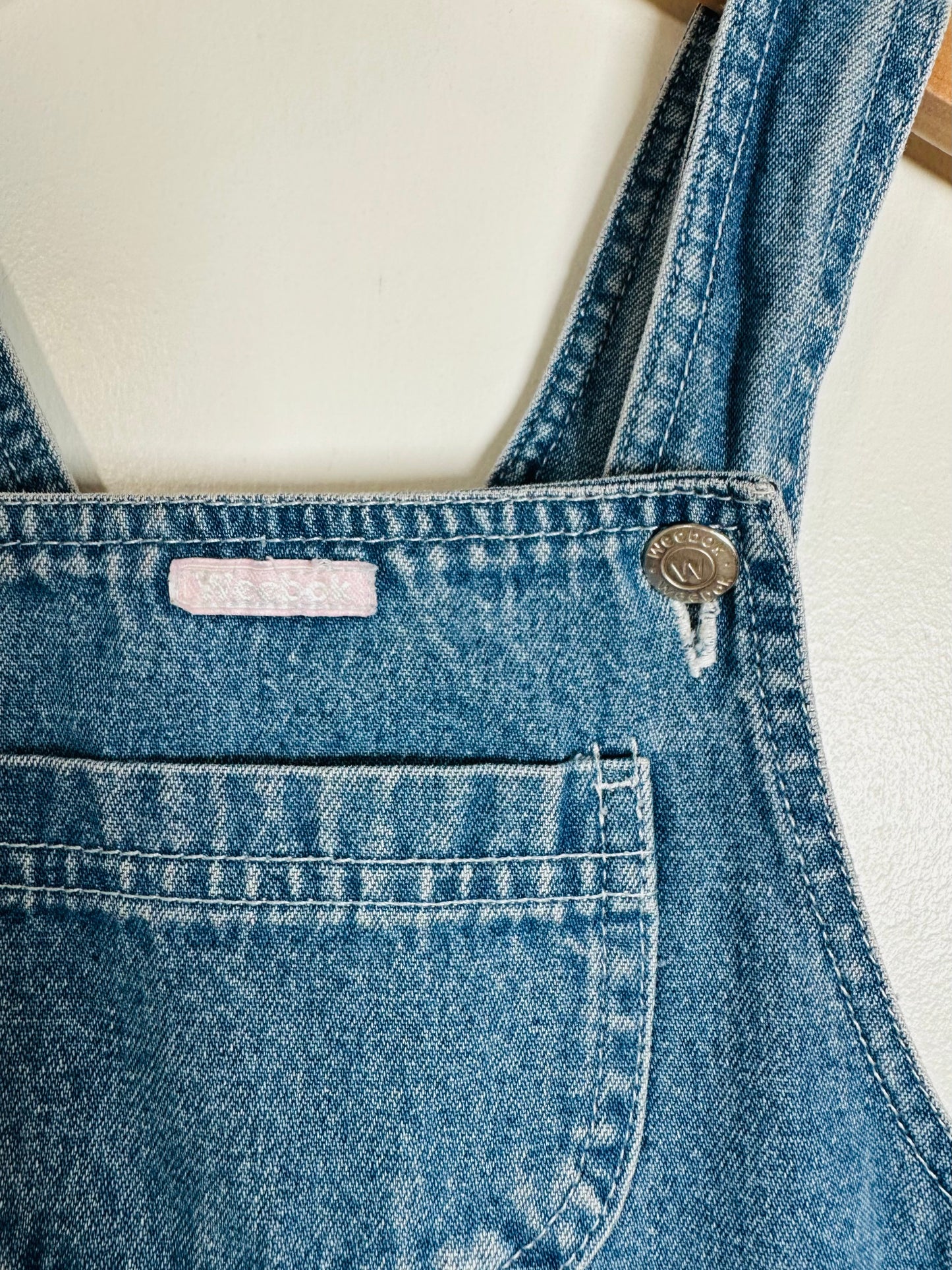 Close-up of blue denim overalls with a brand label on a white background