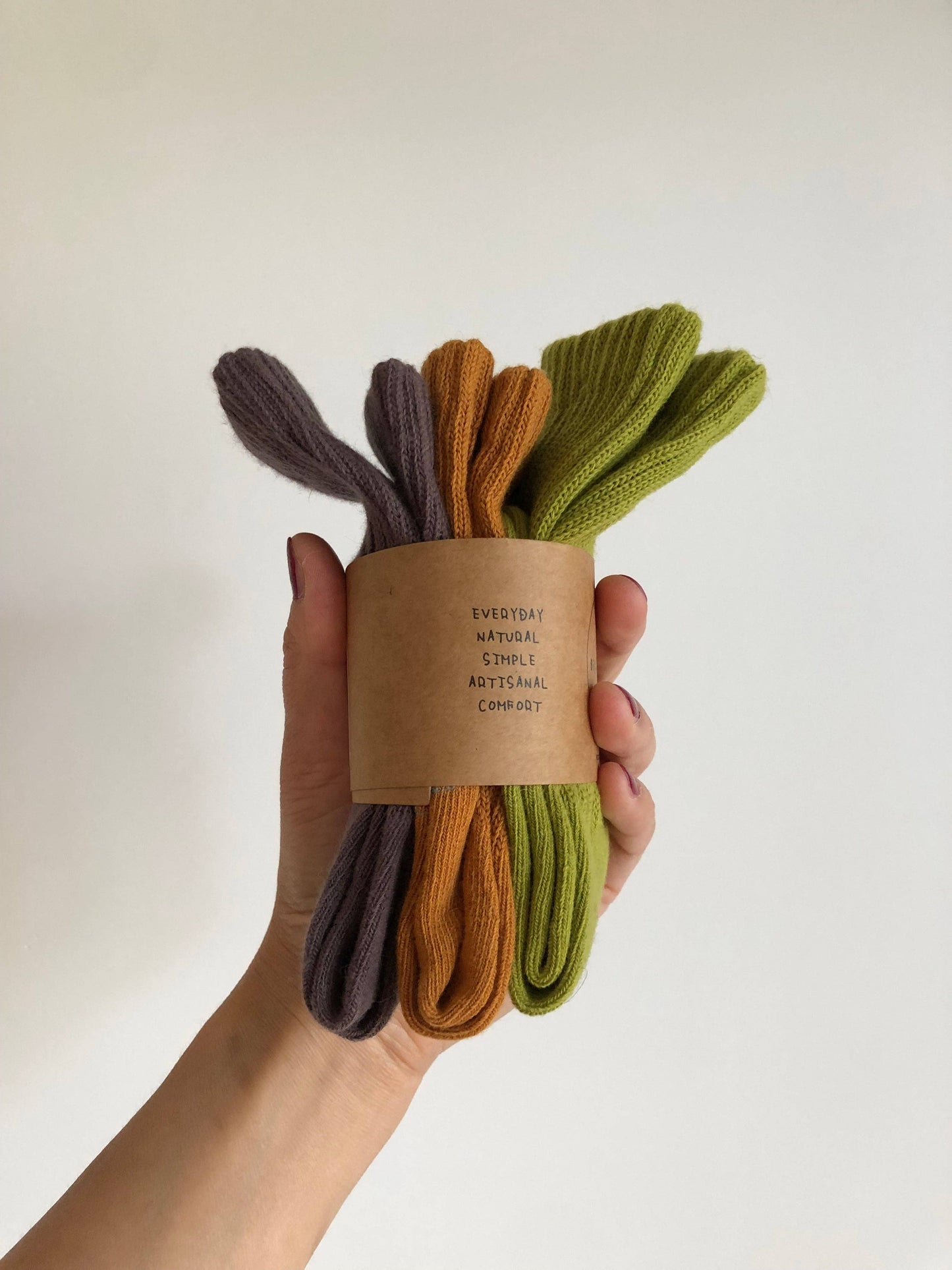 Hand holding a set of three pairs of socks in purple, orange, and green with a brown label.