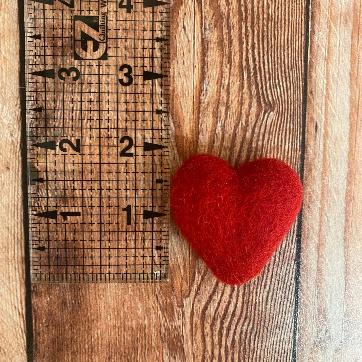Red heart-shaped object next to a wooden ruler on a wooden surface