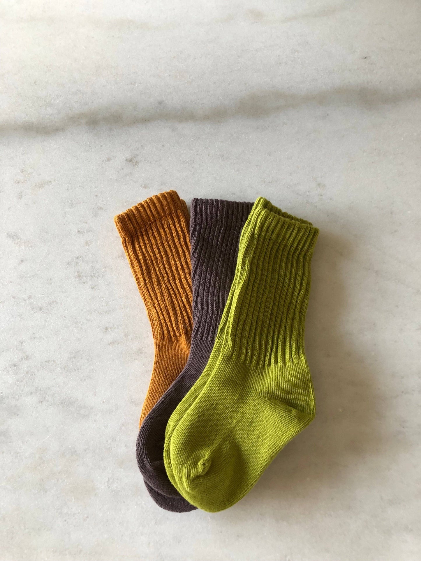 Three socks in brown, purple, and green on a marble surface