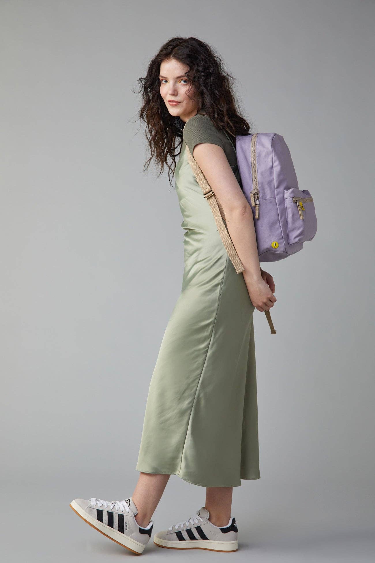 Woman in a green dress with a purple backpack on a gray background