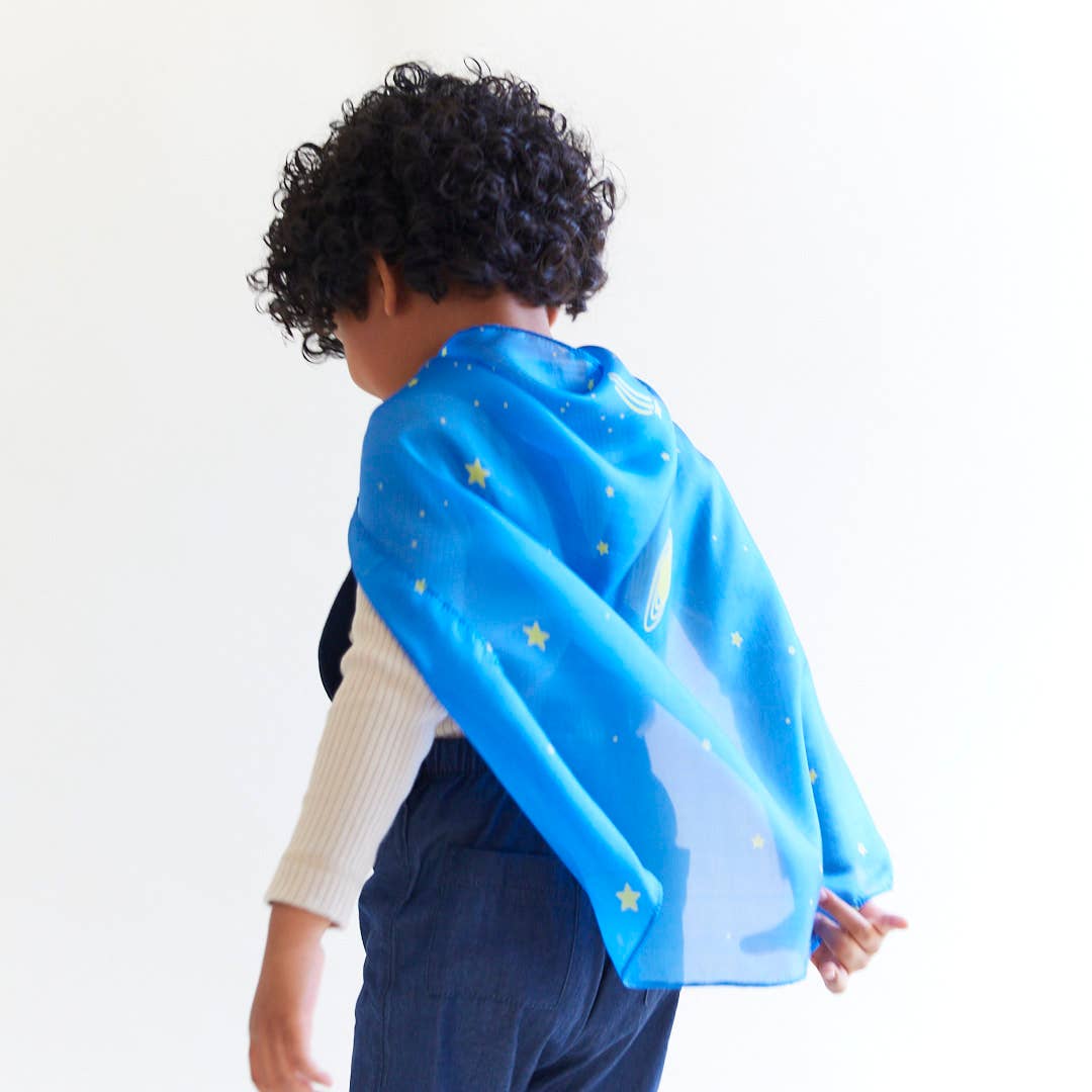 Child wearing a blue cape with star patterns on a white background