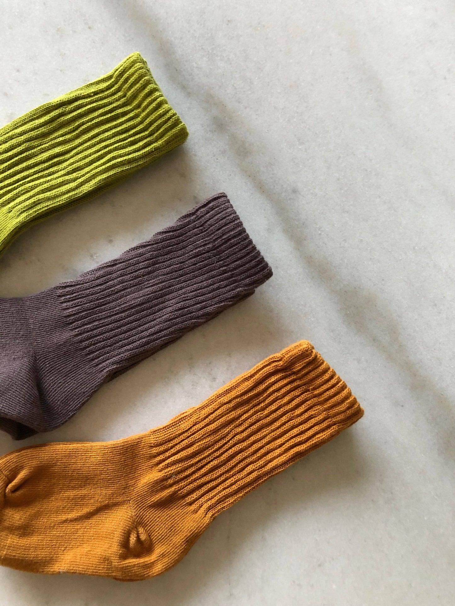 Three pairs of colorful socks (green, purple, orange) on a light fabric background.