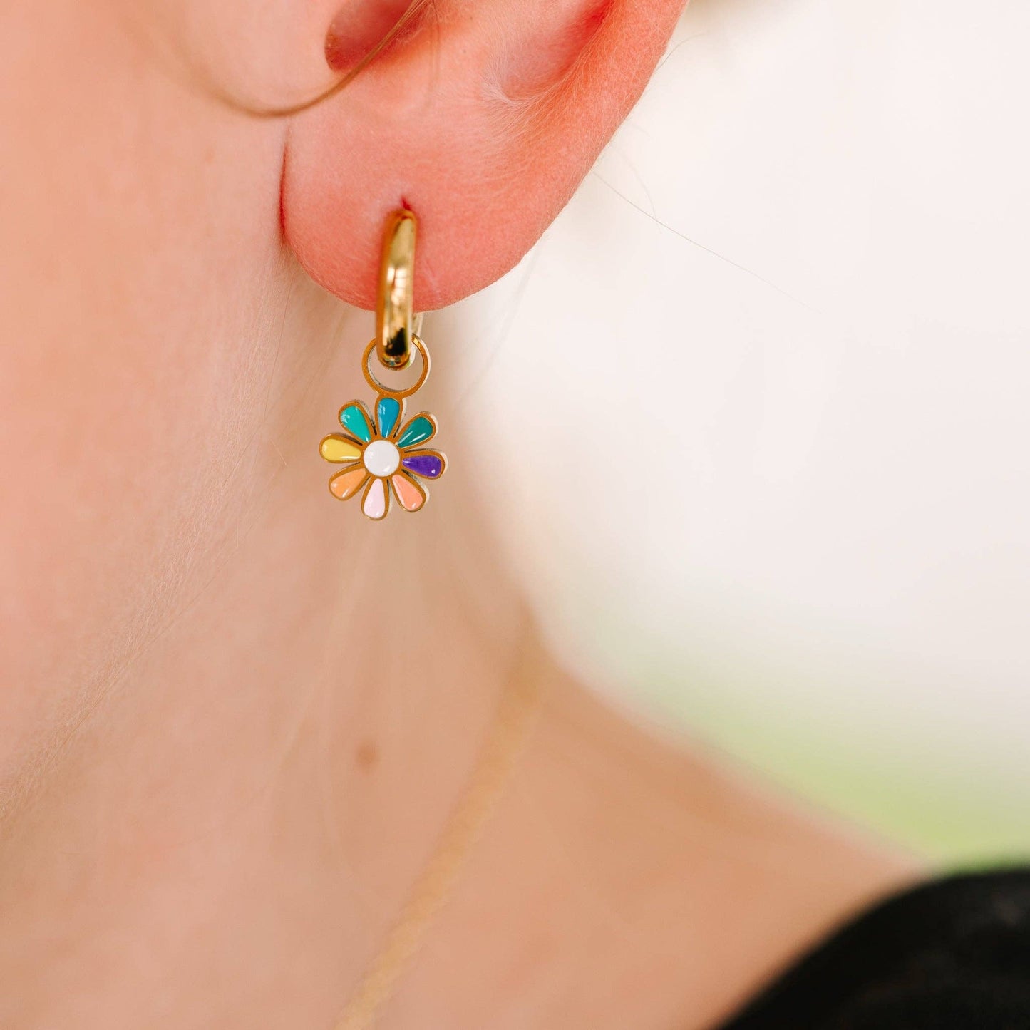 Gold hoop earring with a colorful flower charm worn by a person.