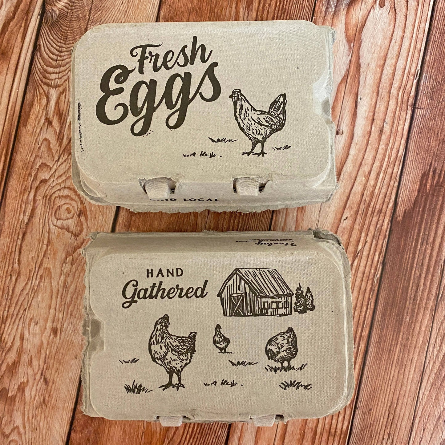 Two cardboard egg boxes with rustic designs and text on a wooden surface