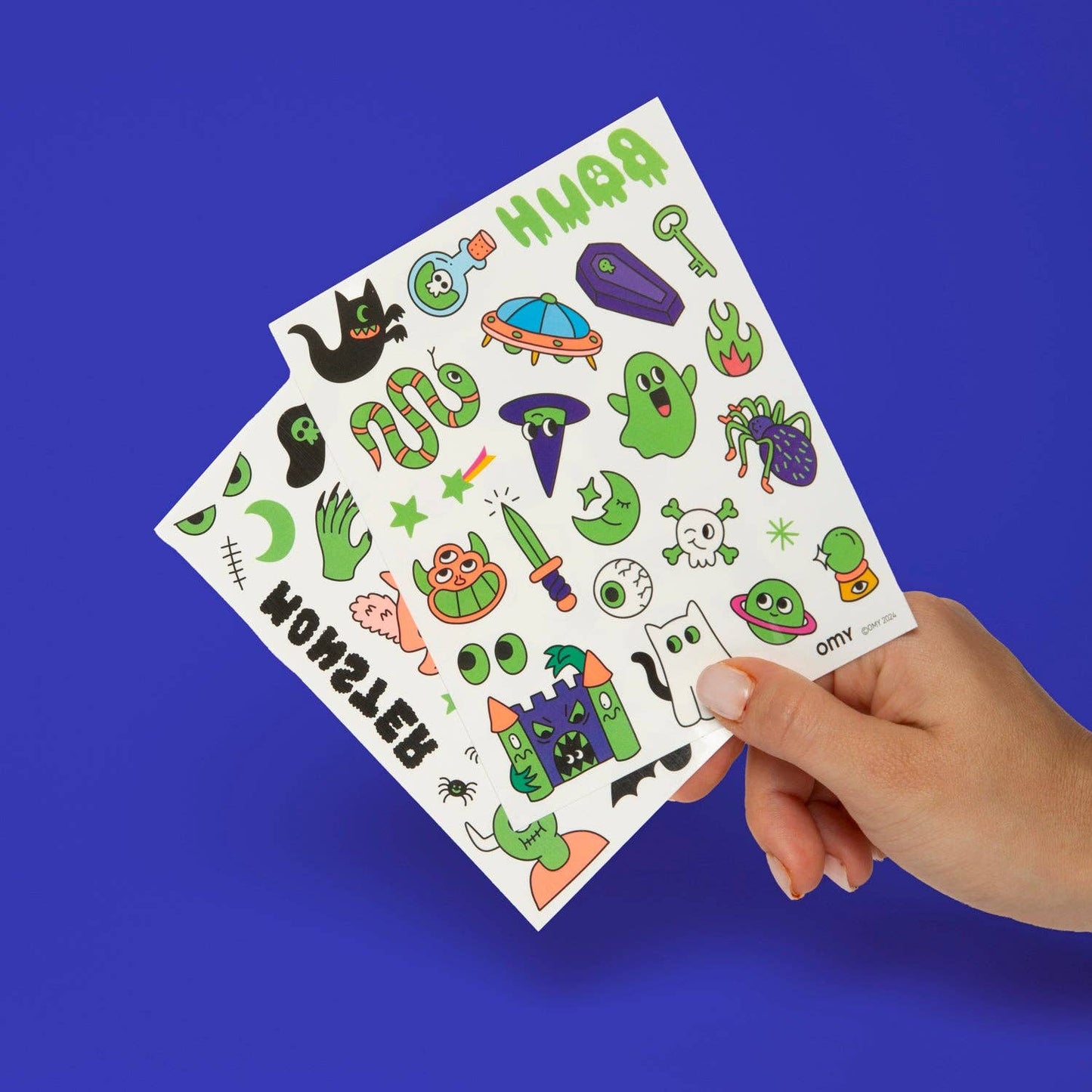Hand holding a sheet of colorful Halloween-themed tattoos against a blue background