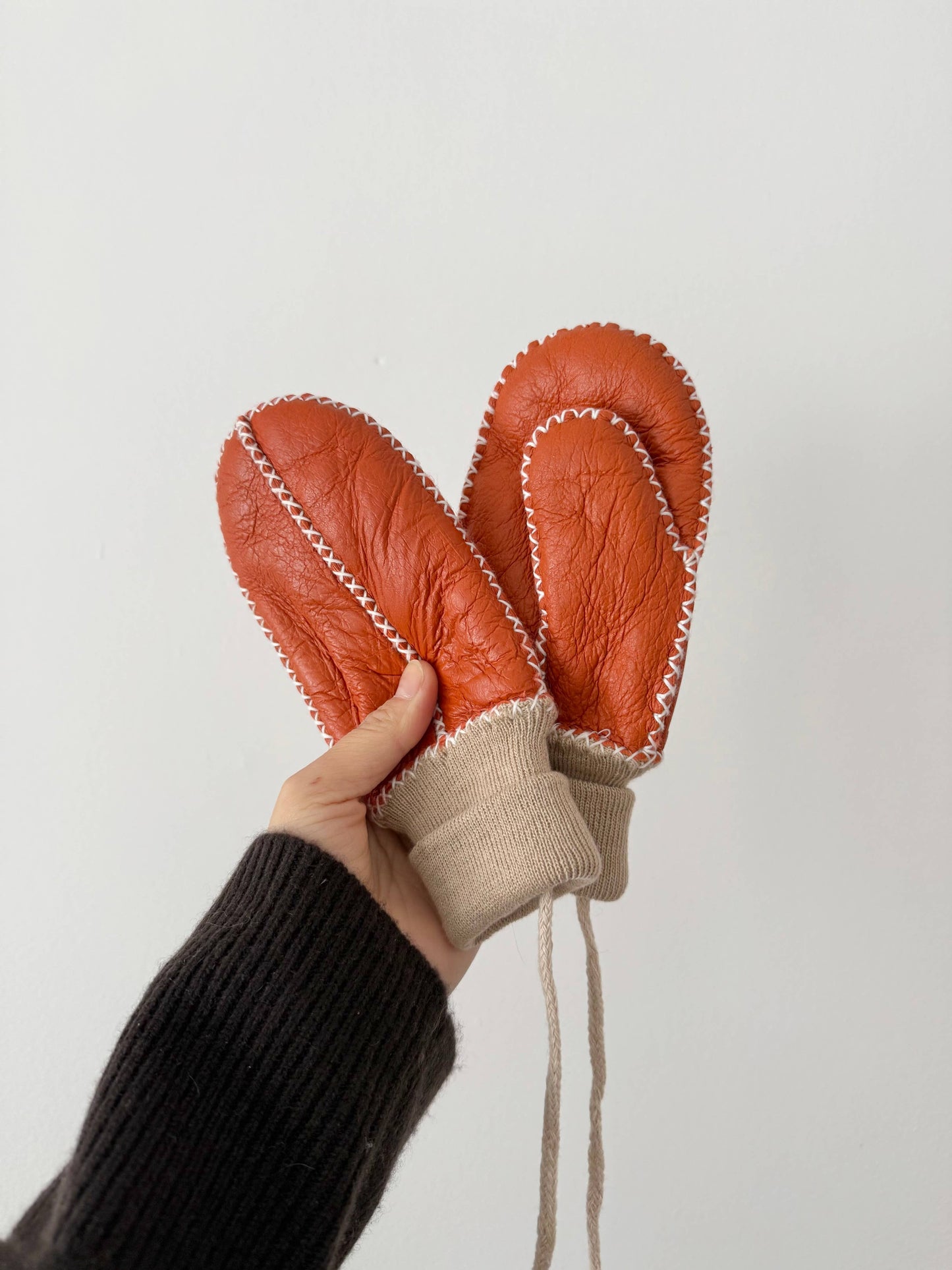 Hand holding a pair of orange leather mittens against a white background