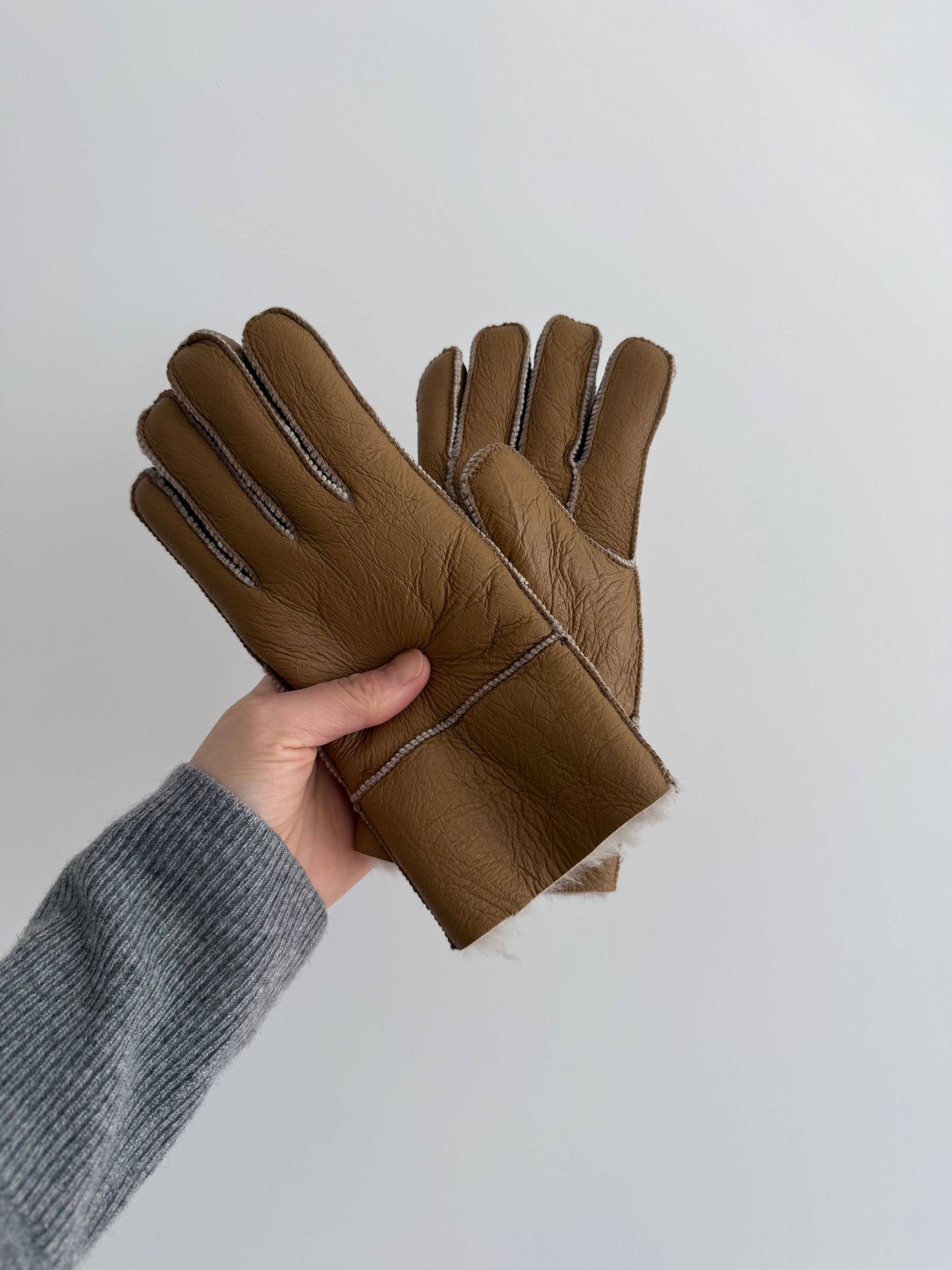 Brown leather gloves held by a hand against a white background