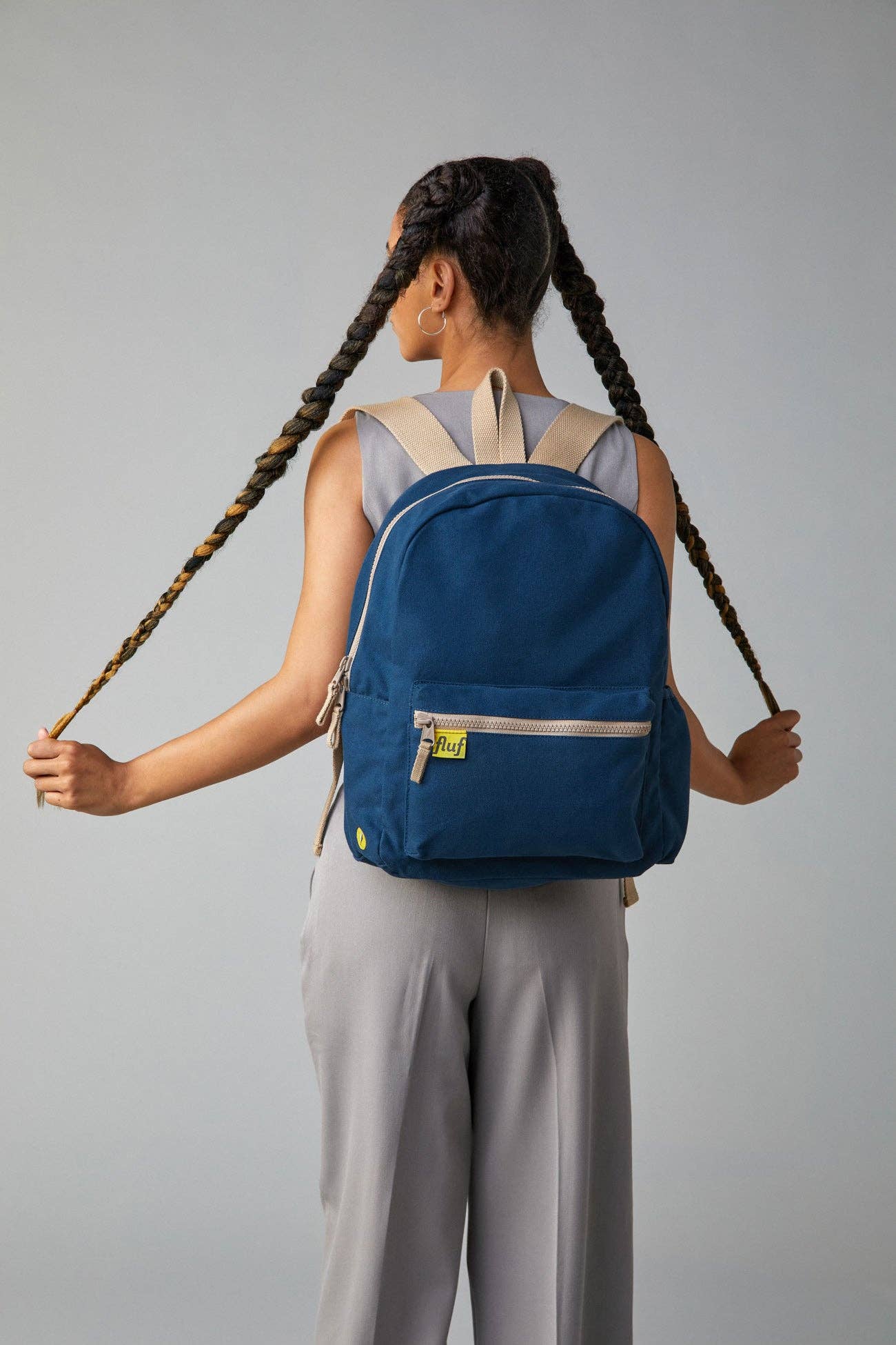 Person wearing a blue backpack with braided hair on a gray background