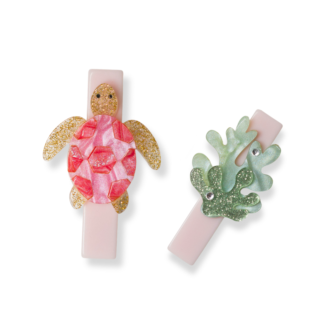 Two hair clips with turtle and leaf designs on a white background