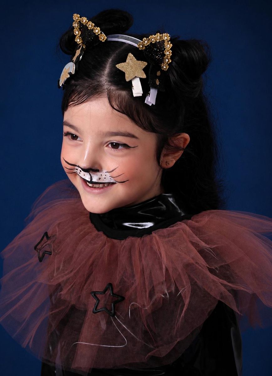 A young girl with cat-inspired Halloween makeup, featuring whiskers and a nose, wearing a black and brown tulle costume with star details and a gold star hair clip against a dark blue background.