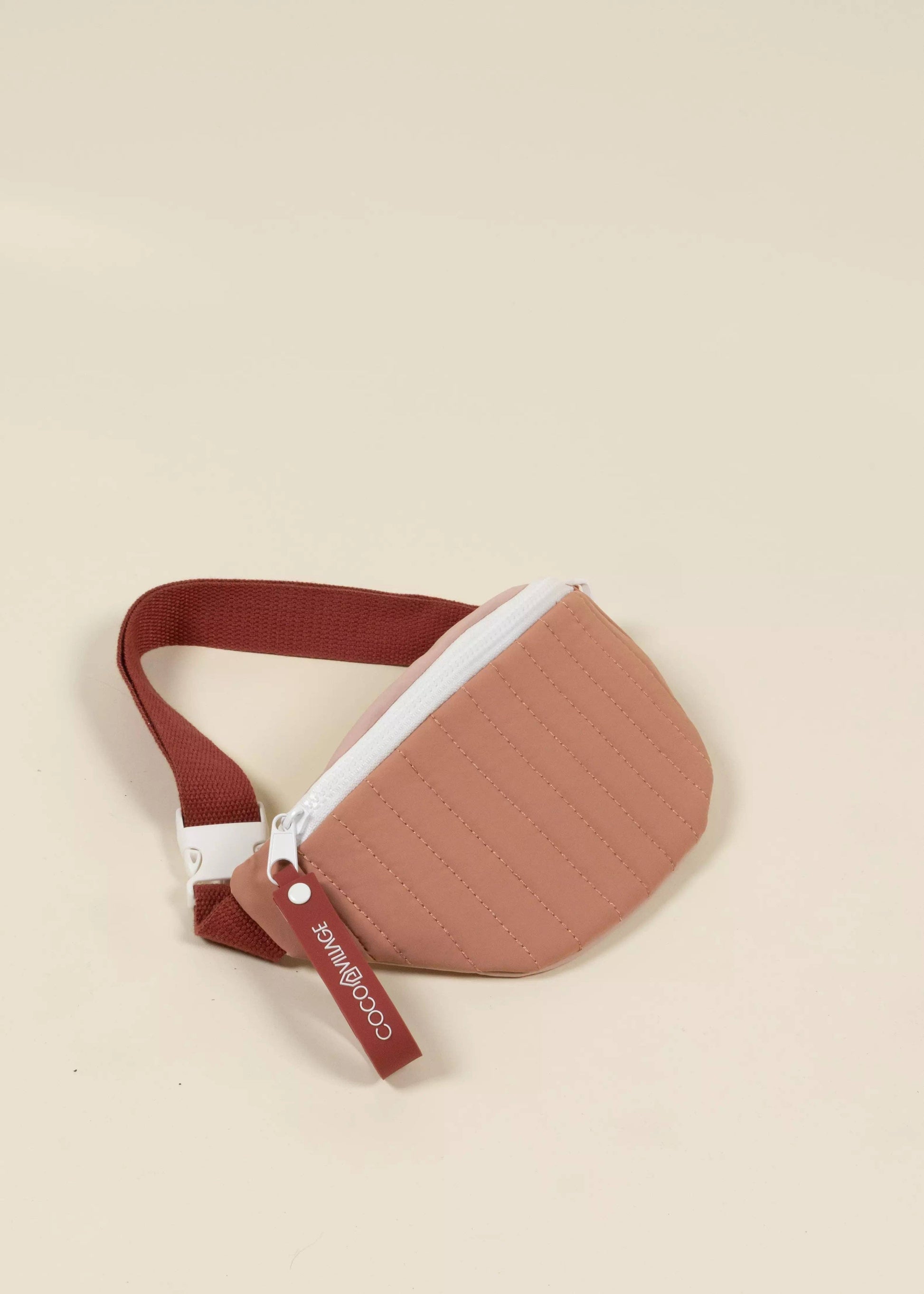 Brown quilted waist bag with a white zipper on a beige background