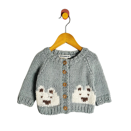Gray knitted cardigan with animal designs on a wooden hanger against a white background