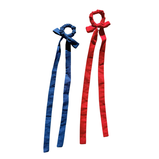 Two fabric hair bows with long ribbon tails, one in blue and one in red, shown on a plain white background.