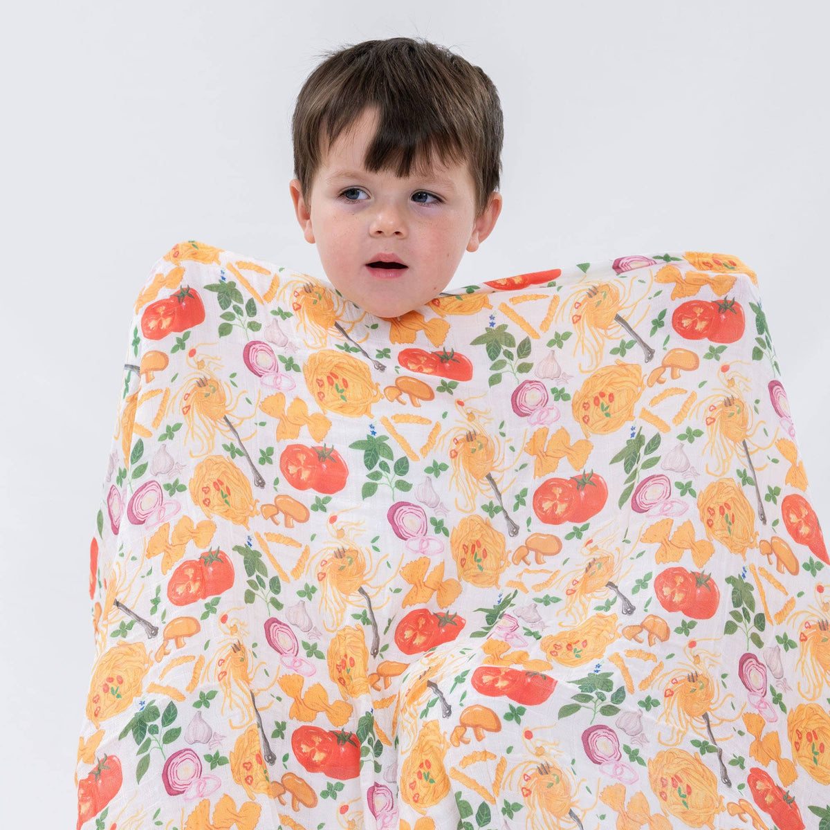 Child wrapped in a pasta patterned blanket with vegetables on a white background
